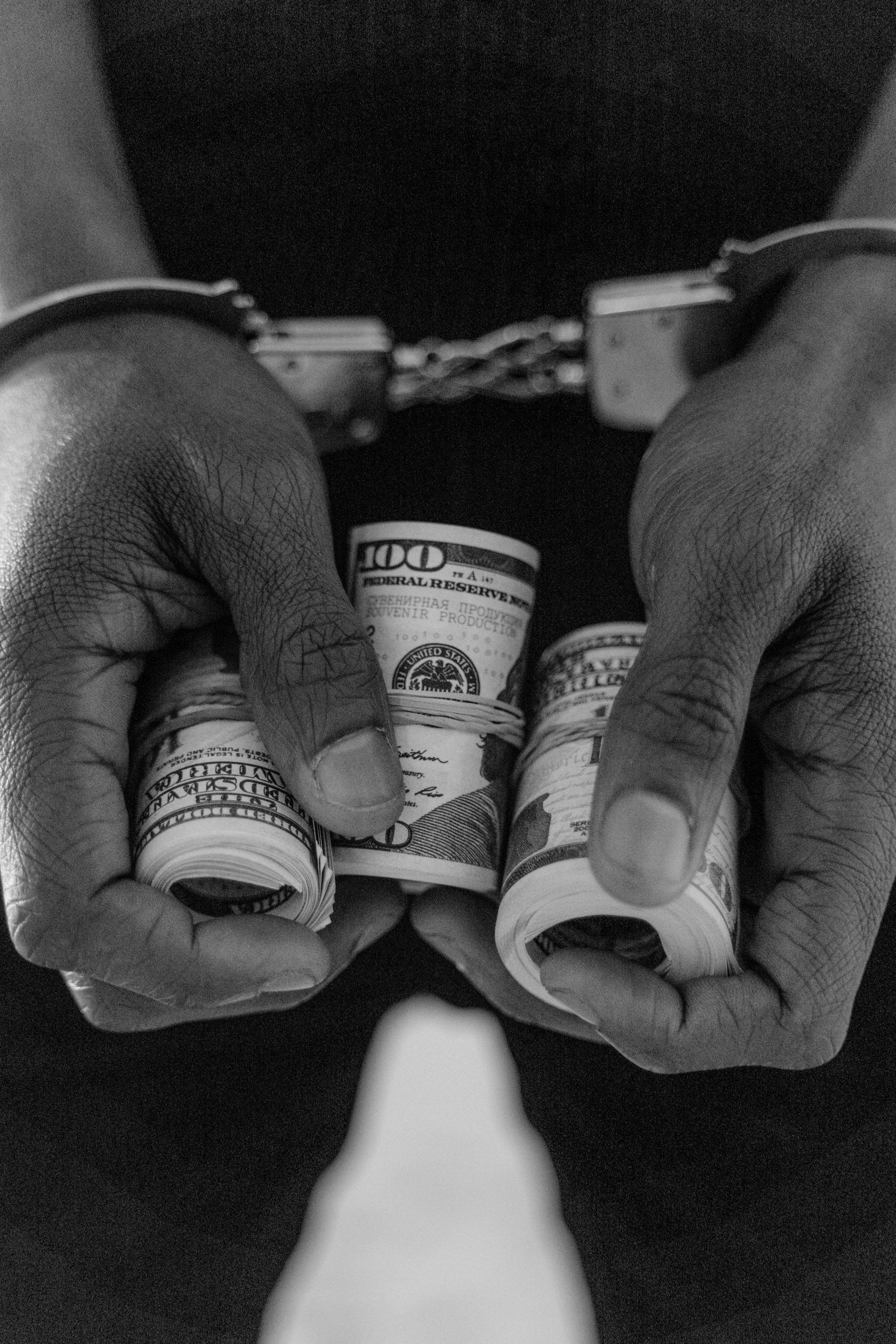 A man in handcuffs is holding two rolls of money in his hands.