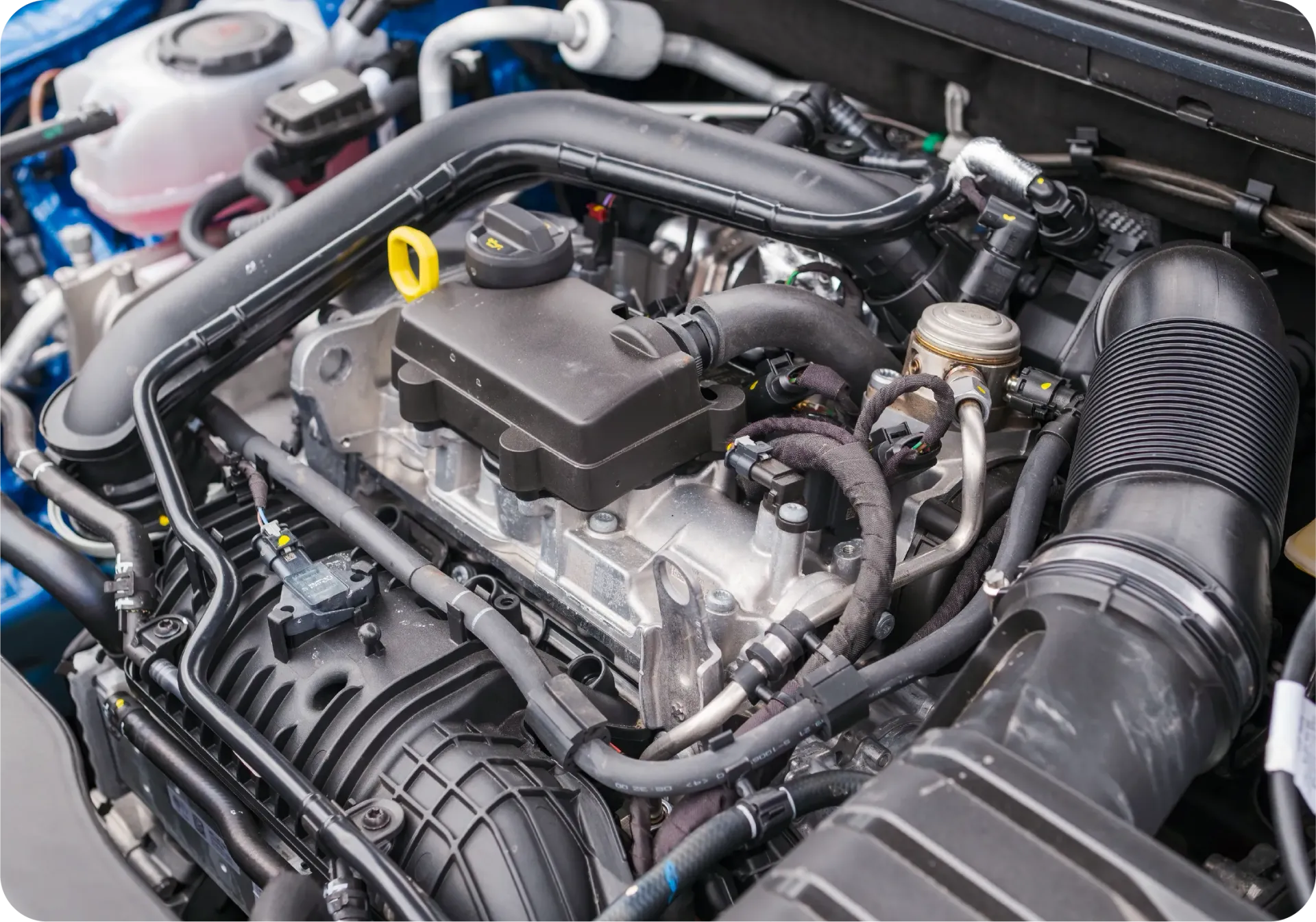 A close-up view of a car's engine bay, showing various mechanical components, hoses, and a yellow oil cap.