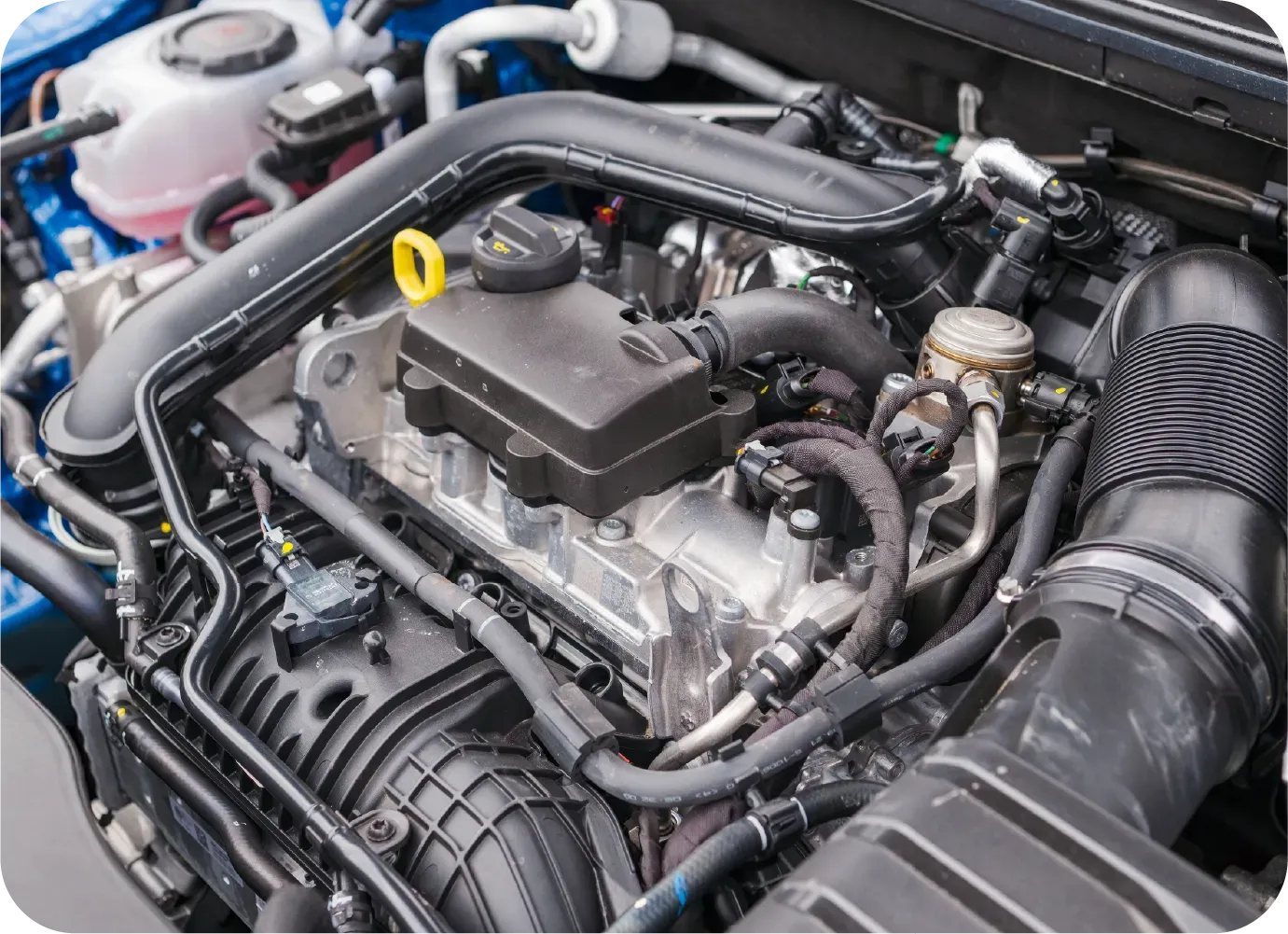A close-up view of a modern internal combustion car engine with black plastic covers and various hoses and components.