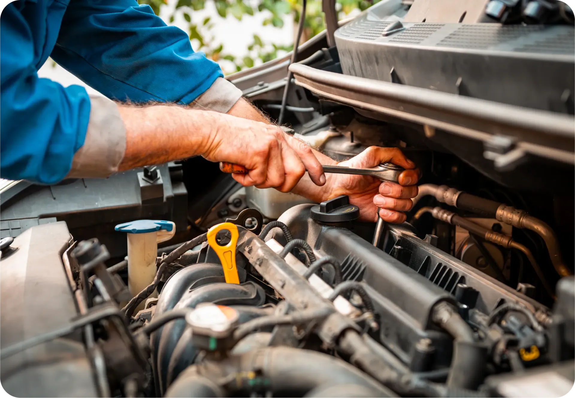 A mechanic wearing a blue uniform uses a wrench to work on a car engine.