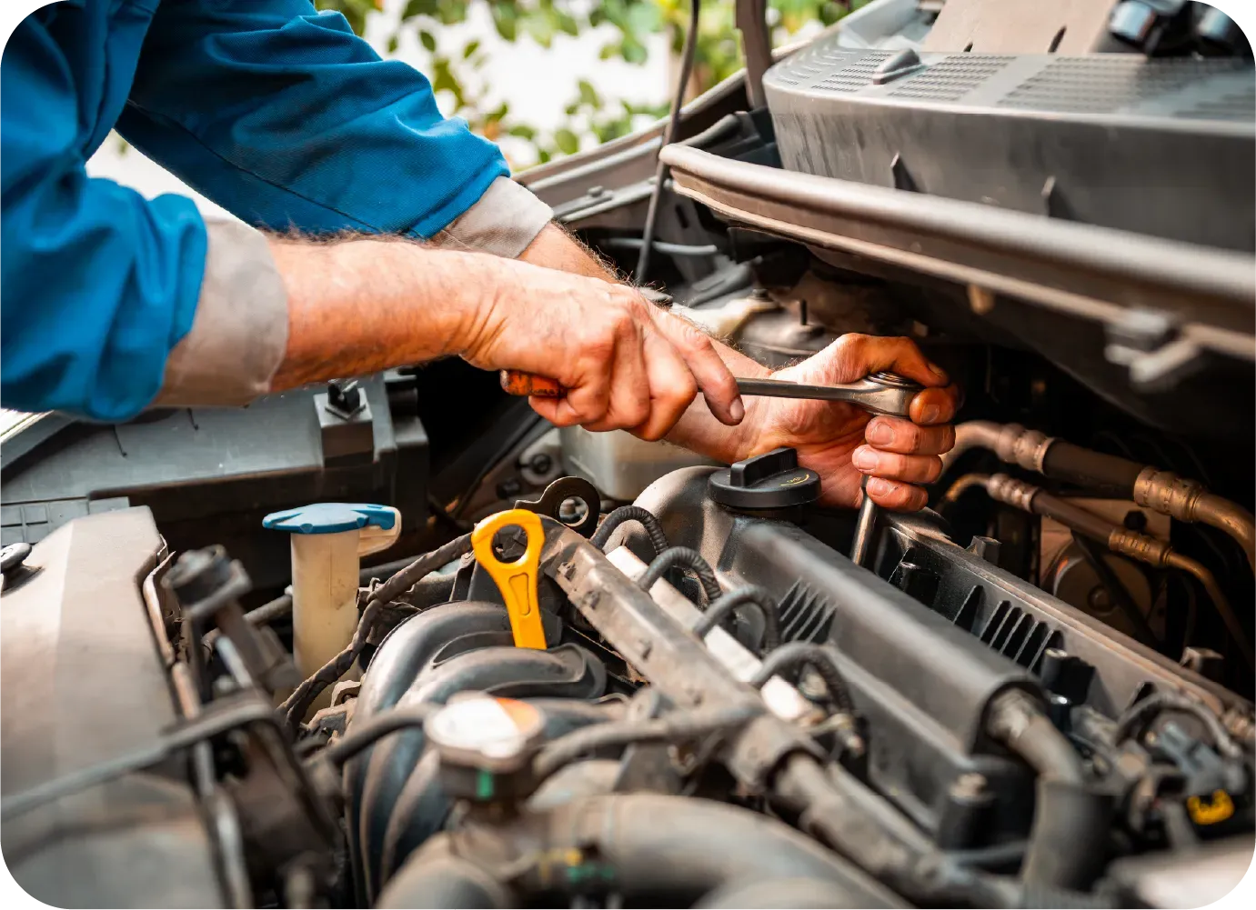 A mechanic in a blue shirt uses a wrench to tighten a bolt on a car engine.