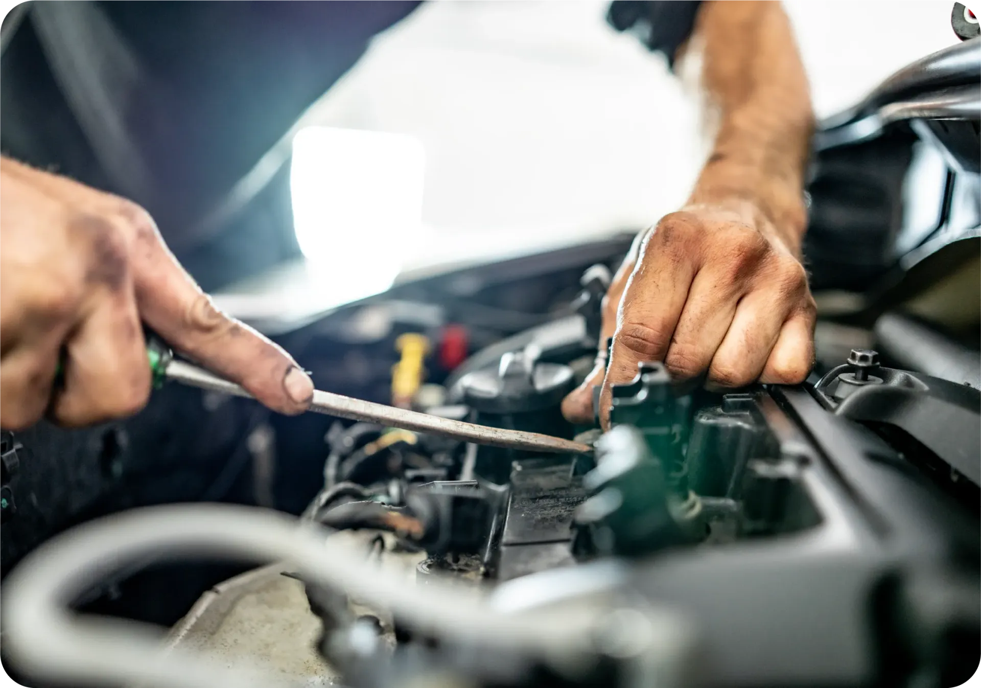 Close-up of a mechanic's hands using a screwdriver to perform maintenance on a car engine.