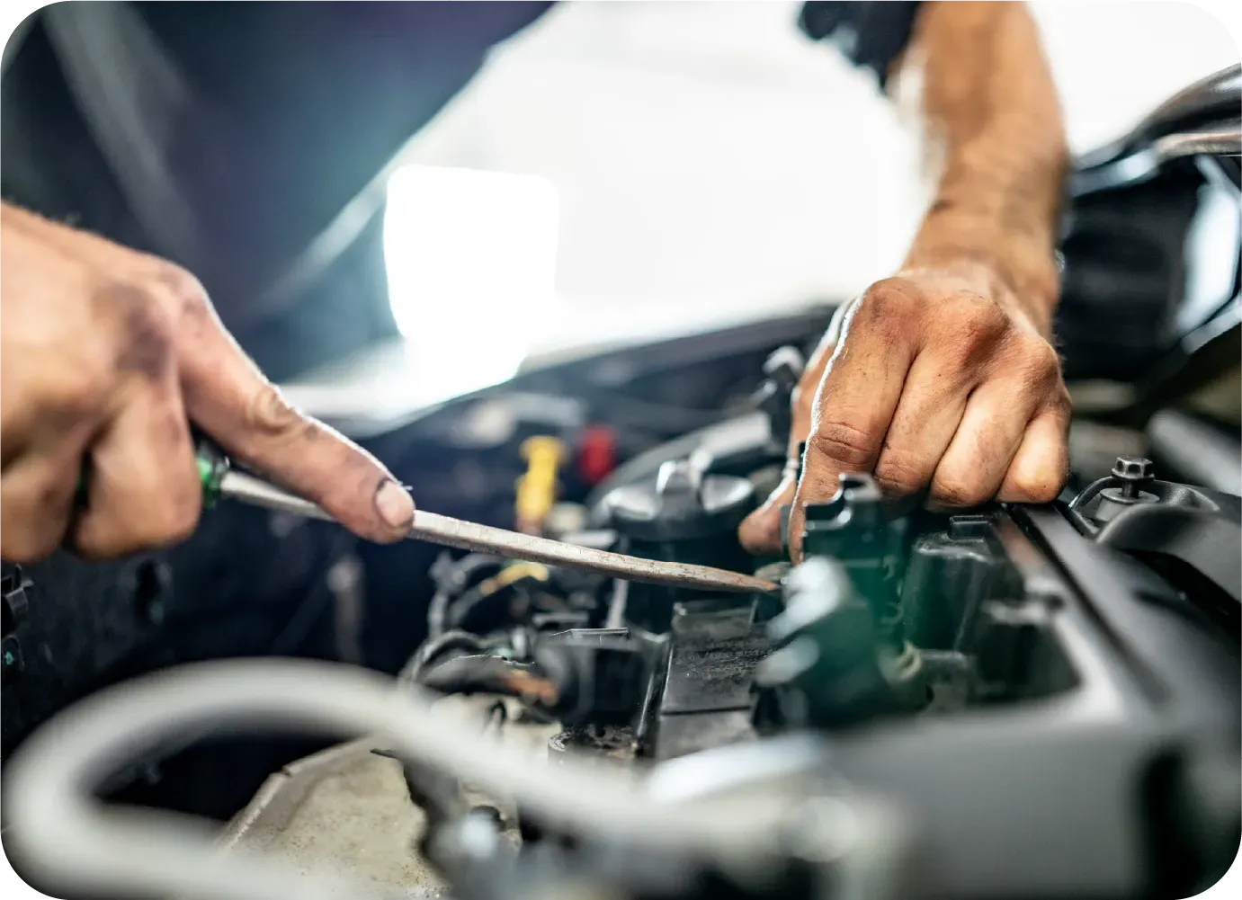 A mechanic uses a screwdriver to work on a car engine in a repair shop.