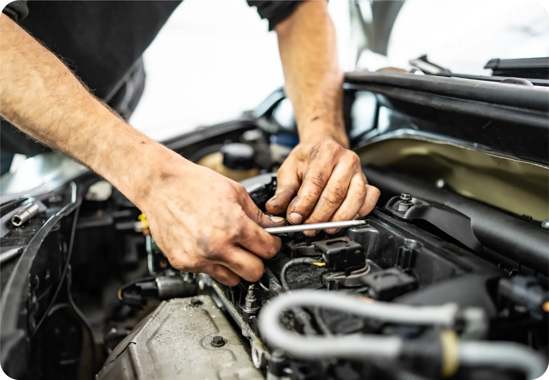 A mechanic working on the engine of a car, using a wrench to tighten or adjust components under the hood.