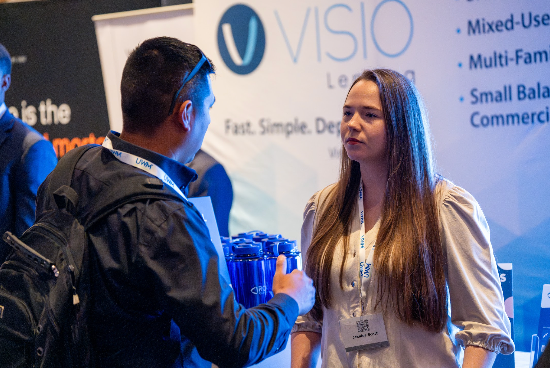 A man and a woman are talking in front of a sign that says visio