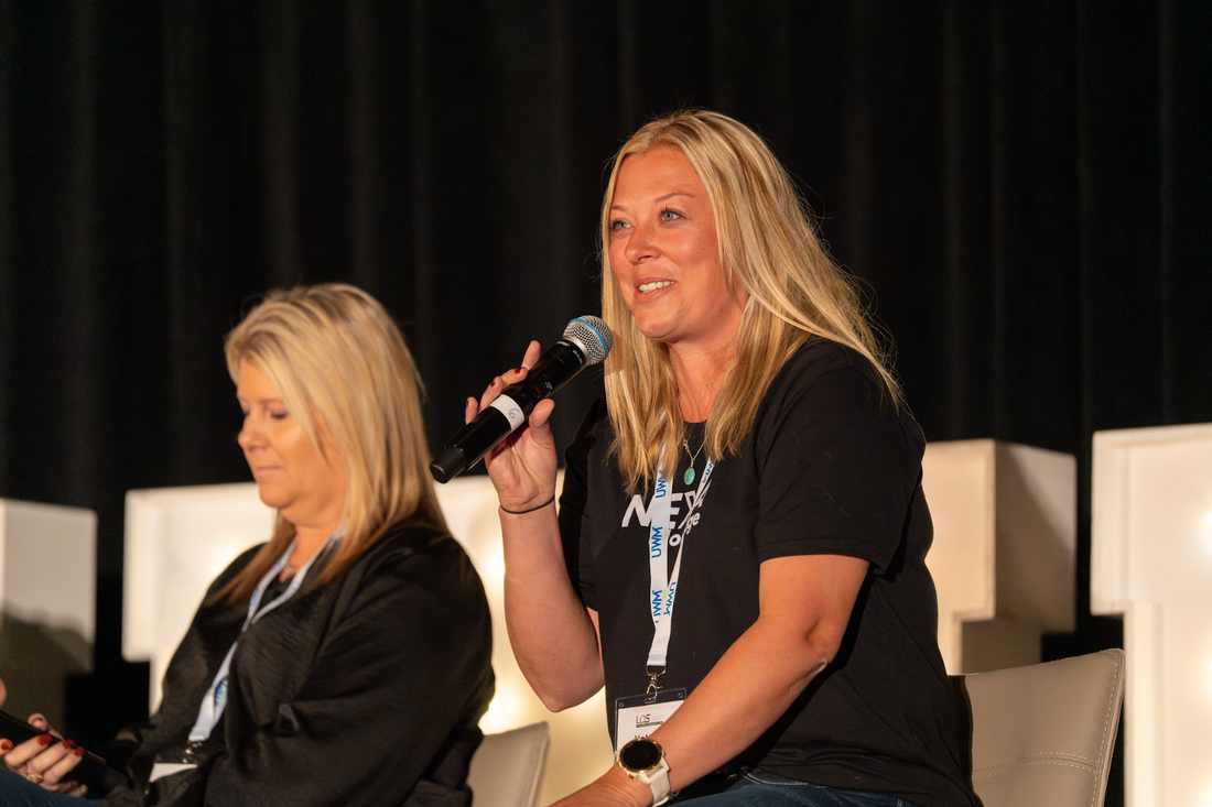 Two women are sitting on a stage talking into microphones.