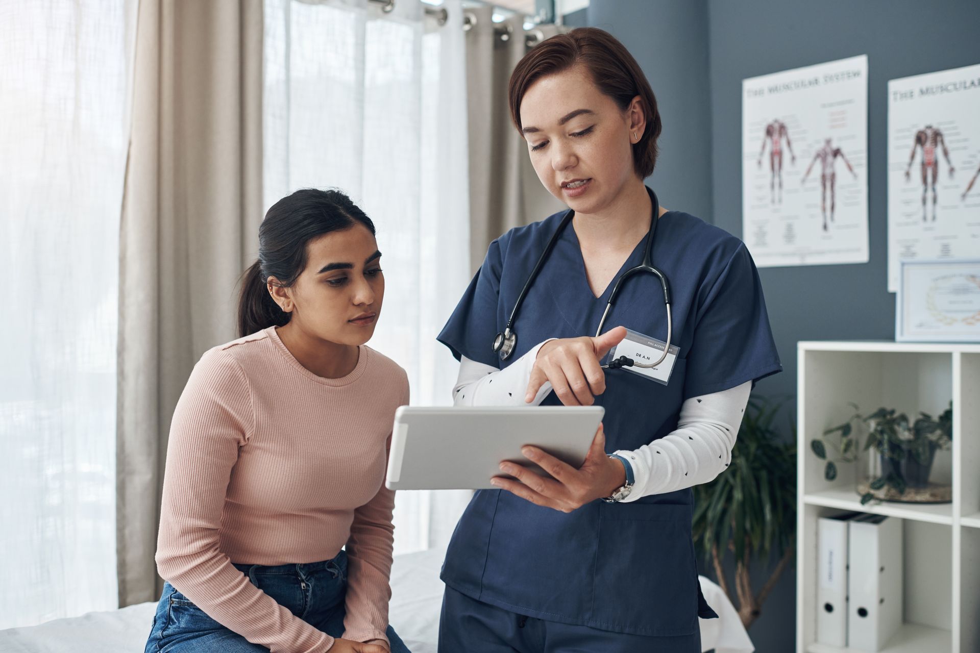 A doctor talking to a patient and showing her information on a tablet in an office.