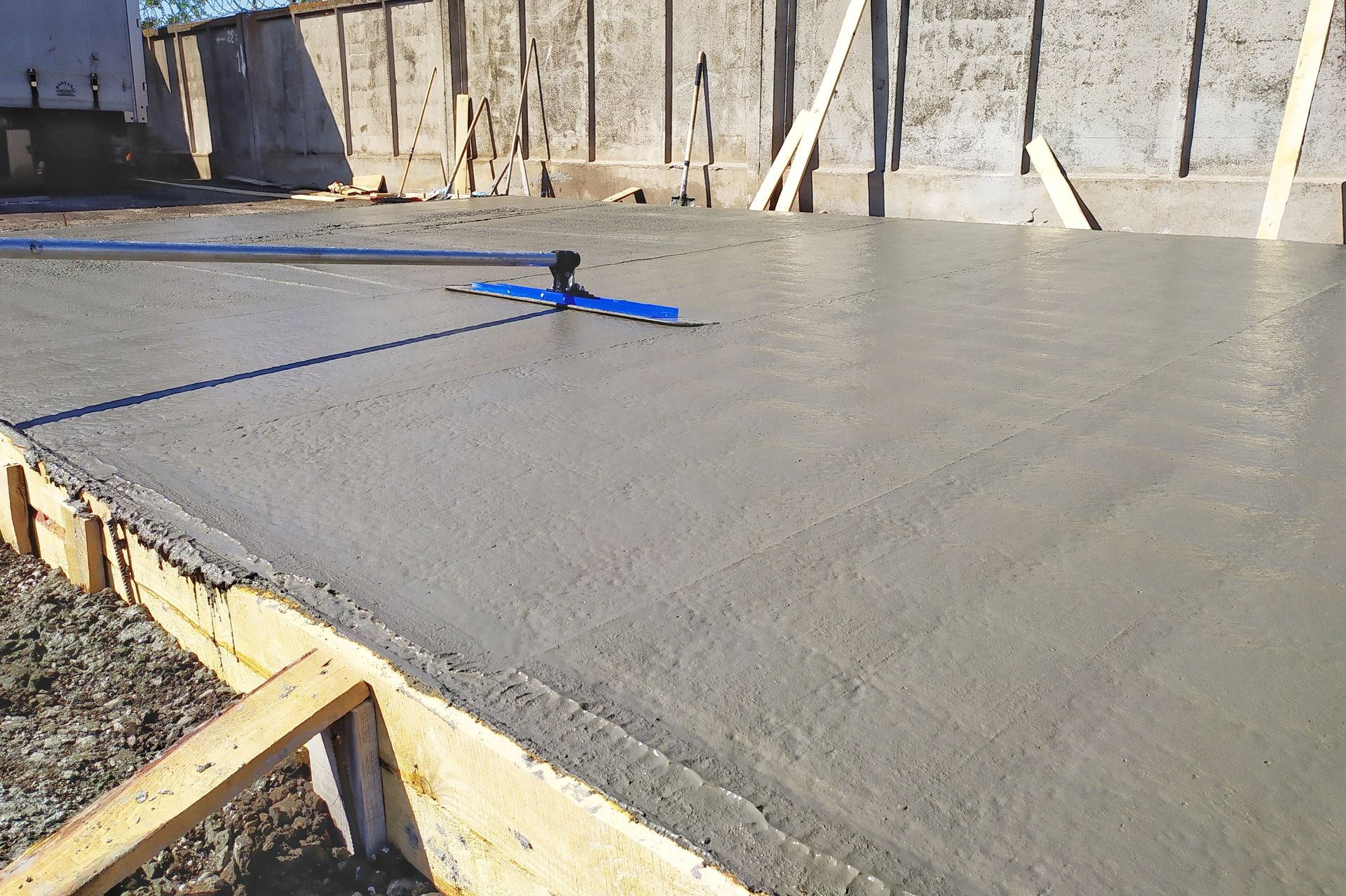 Freshly poured concrete slab being leveled with a bull float in wood forms.