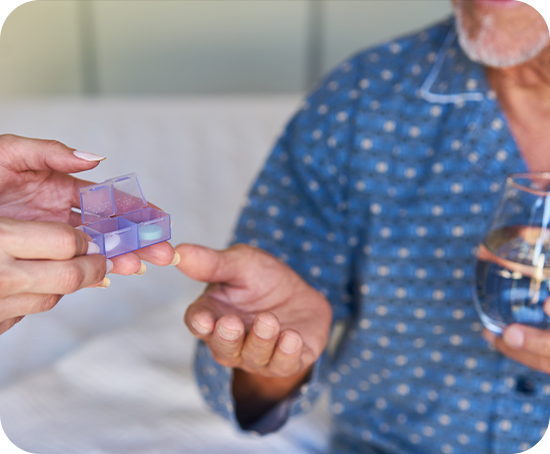 A woman is giving an elderly man a pill box and a glass of water.