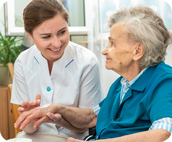 A nurse is holding the hand of an elderly woman in a wheelchair.