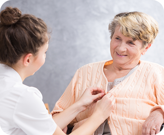 A nurse is helping an elderly woman with her jacket.