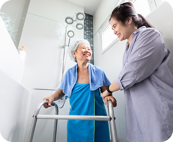 A woman is helping an elderly woman use a walker in the bathroom.