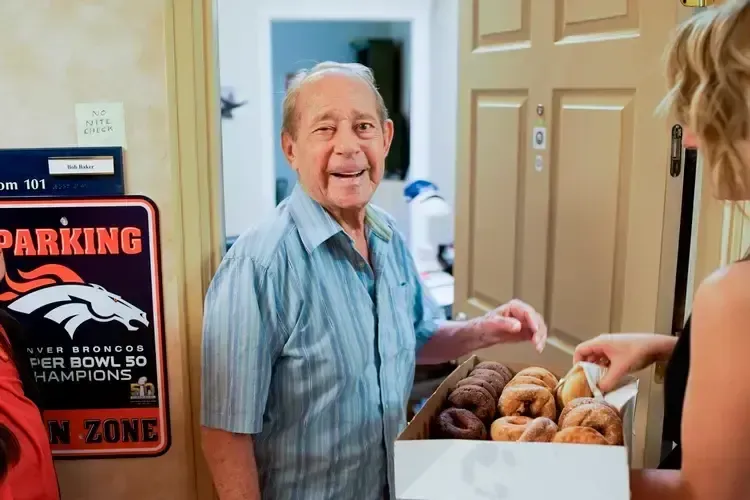 A woman is giving an elderly man a box of donuts.