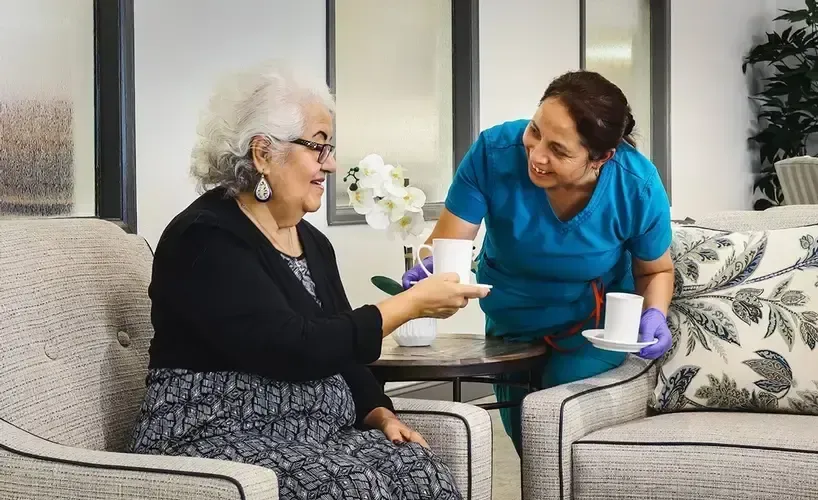 A nurse is serving an elderly woman a cup of coffee.