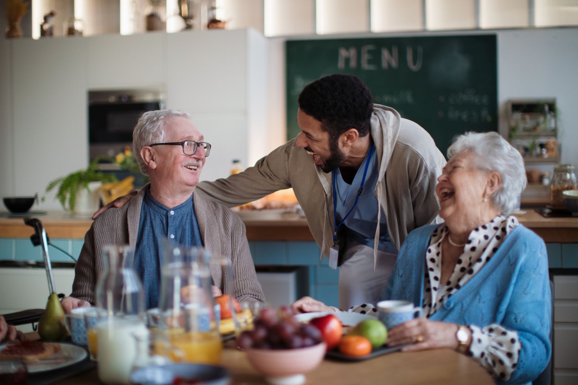 A man is talking to two elderly people sitting at a table.