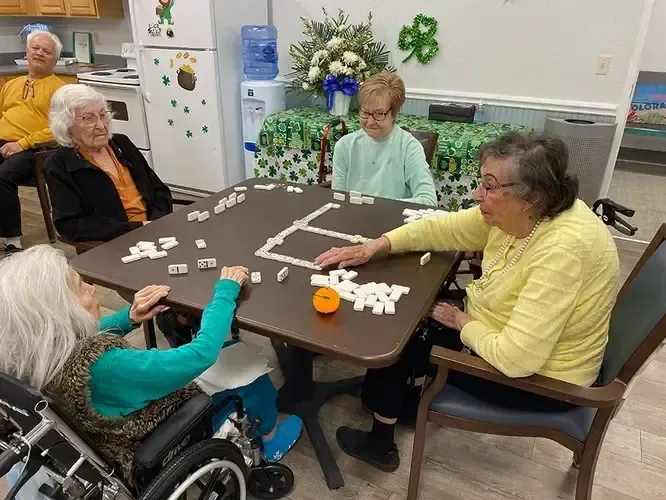 A group of elderly women are sitting around a table playing dominoes.