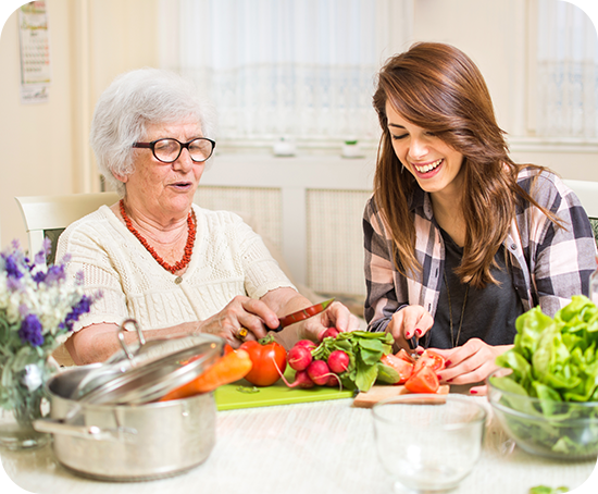 A young woman is helping an older woman cut vegetables at a table.