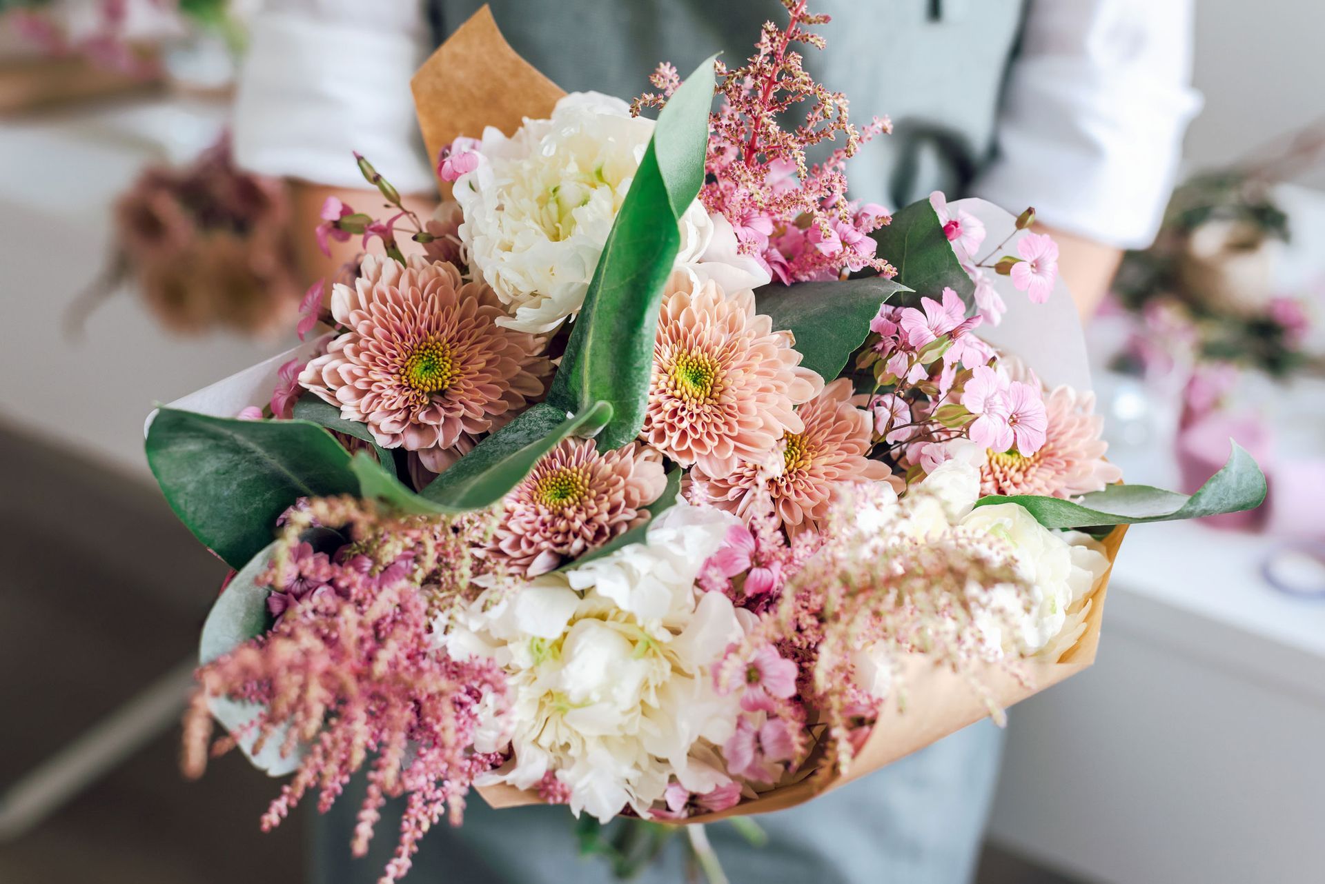 Person holding a bouquet of pink, white, and peach flowers wrapped in brown paper.