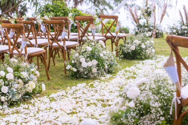 Wedding ceremony setup with wooden chairs and white floral decorations on green grass.