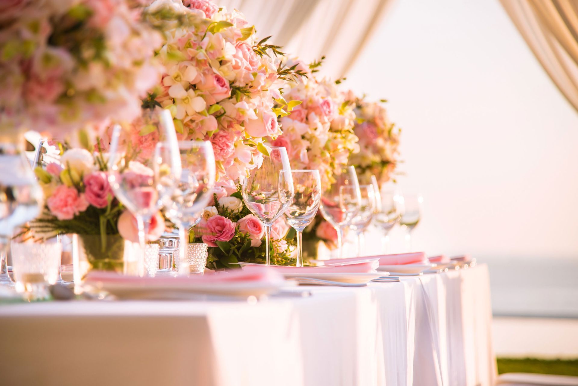 Wedding reception table with floral arrangements, glasses, and pink accents.