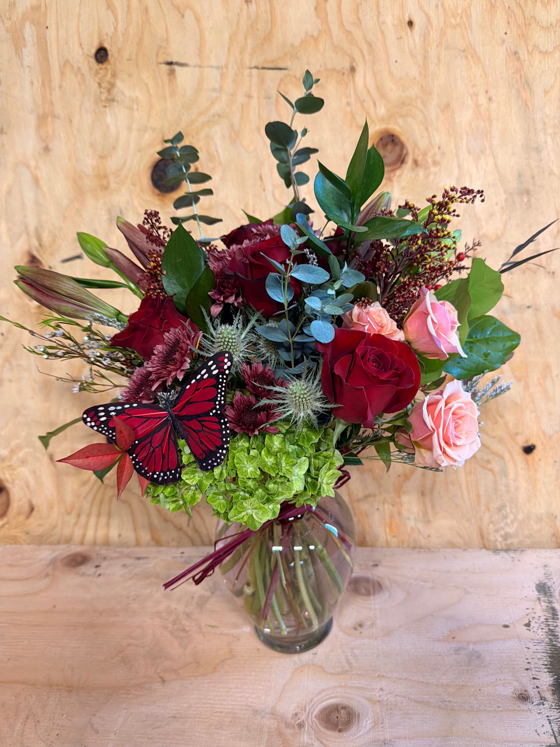 A vase of flowers with butterflies, lit up with fairy lights on a wooden table.