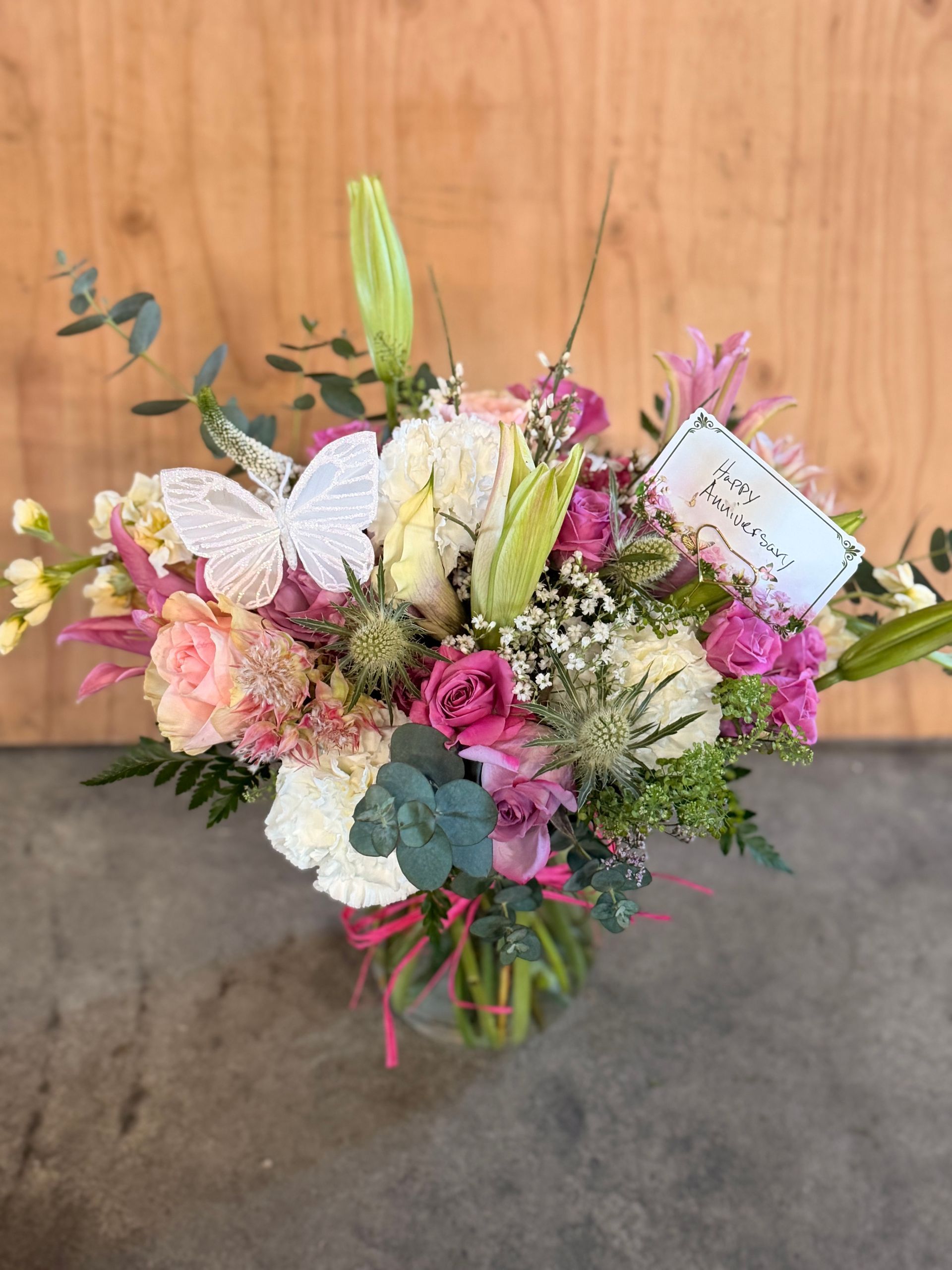 Floral arrangement of purple roses, alstroemeria, and blue delphiniums in a glass vase.