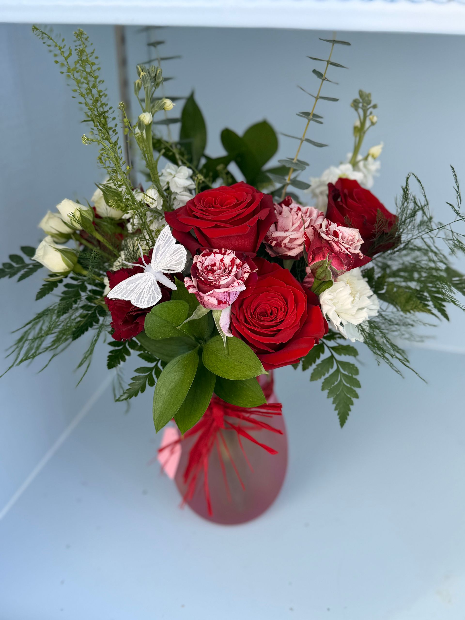 Floral arrangement of purple roses, alstroemeria, and blue delphiniums in a glass vase.