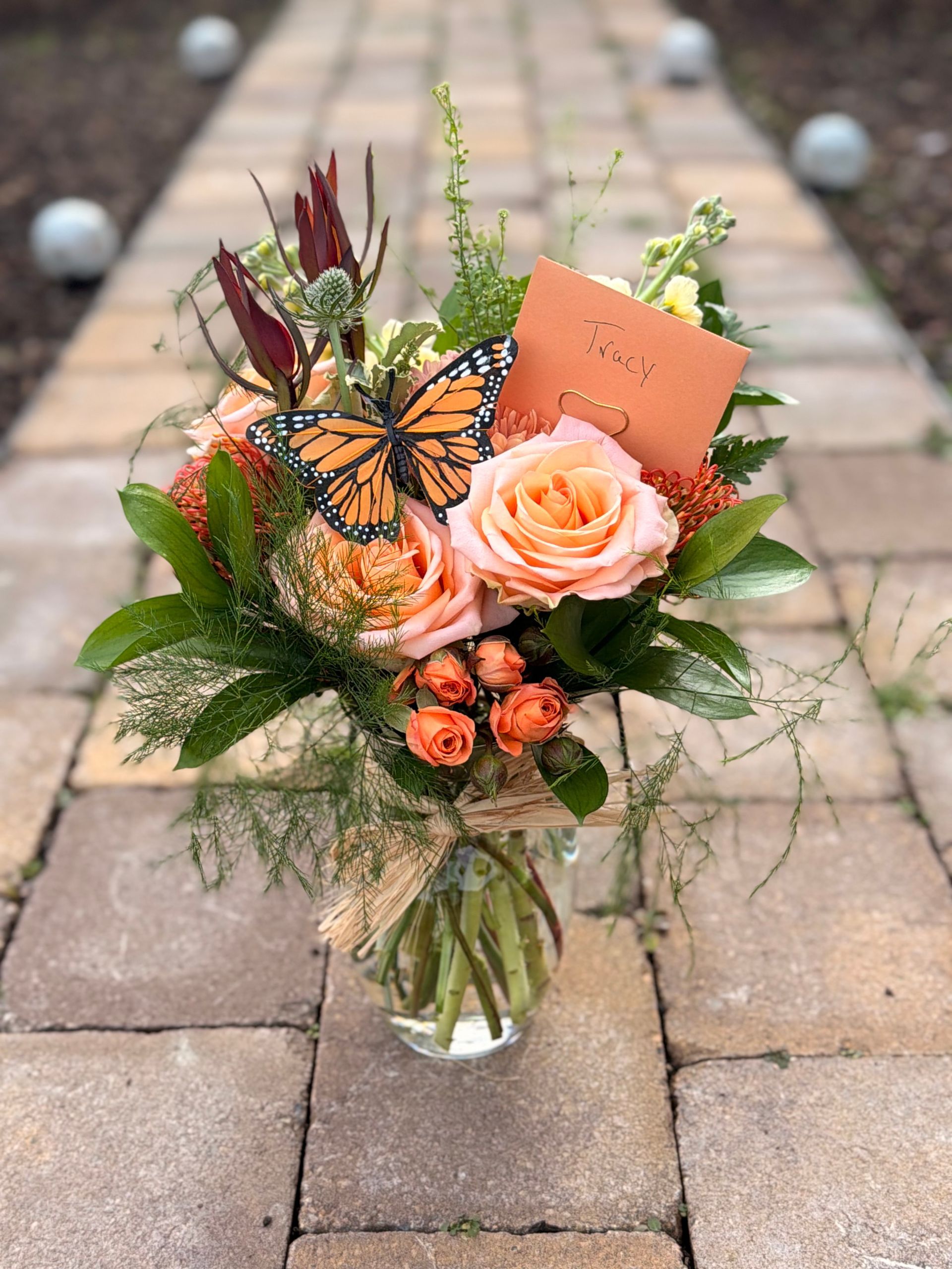 Purple rose floral arrangement in glass vase with butterfly accents on a wooden surface.