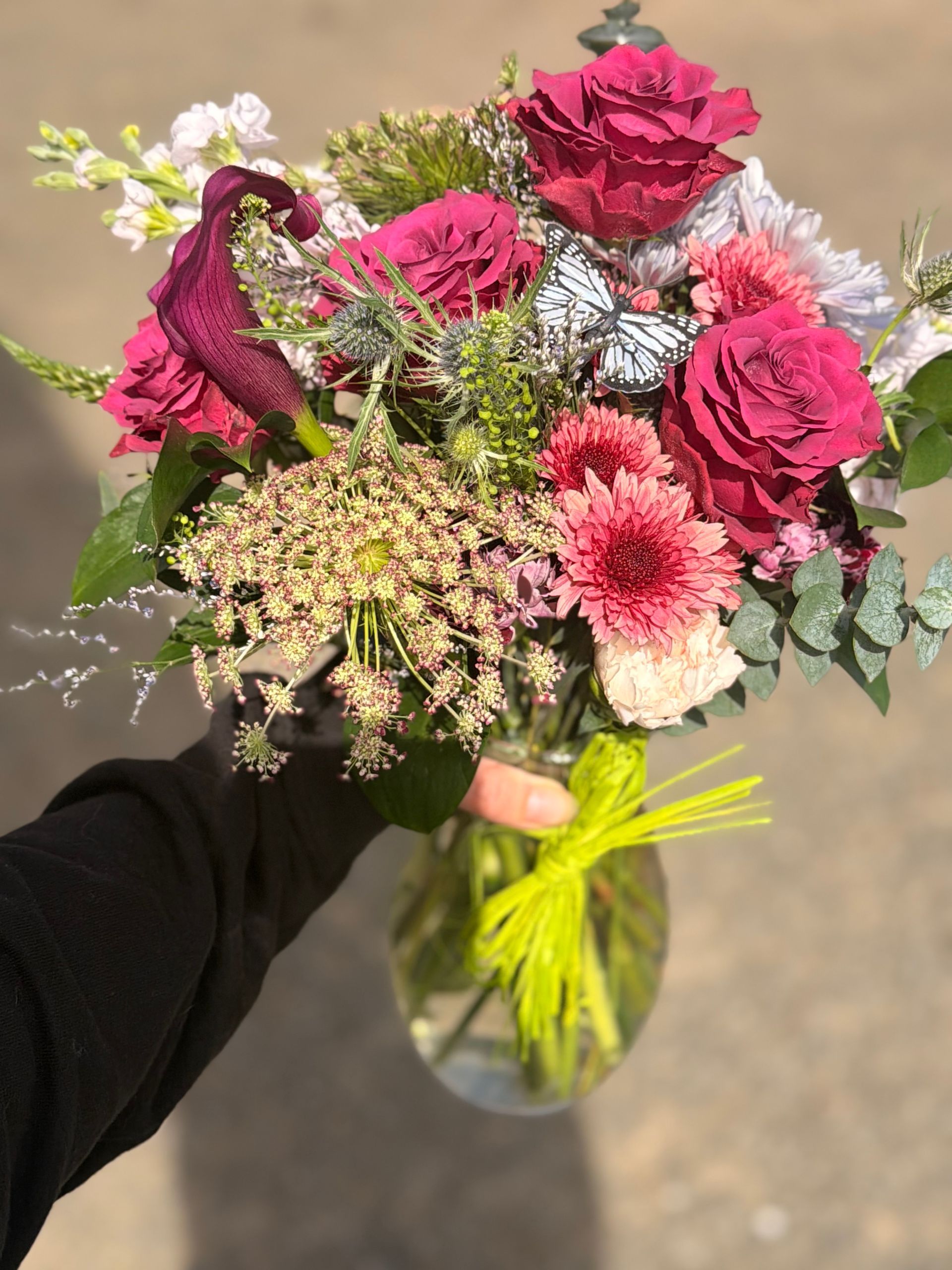 Purple rose floral arrangement in glass vase with butterfly accents on a wooden surface.