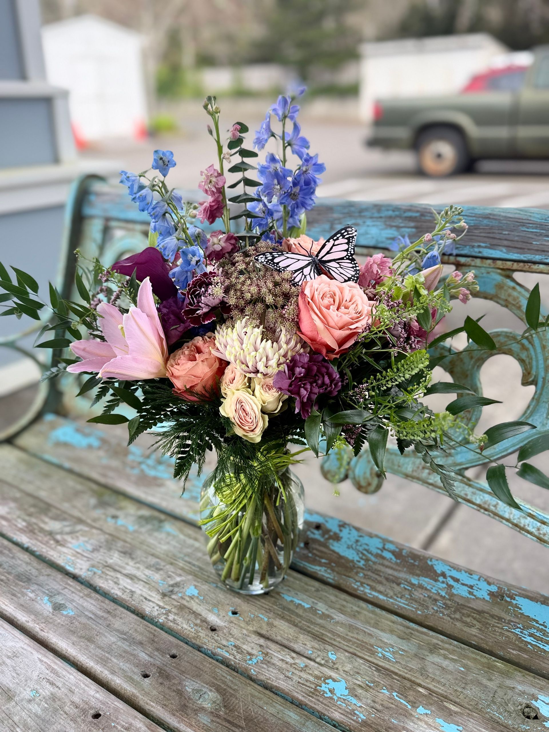 Purple rose floral arrangement in glass vase with butterfly accents on a wooden surface.