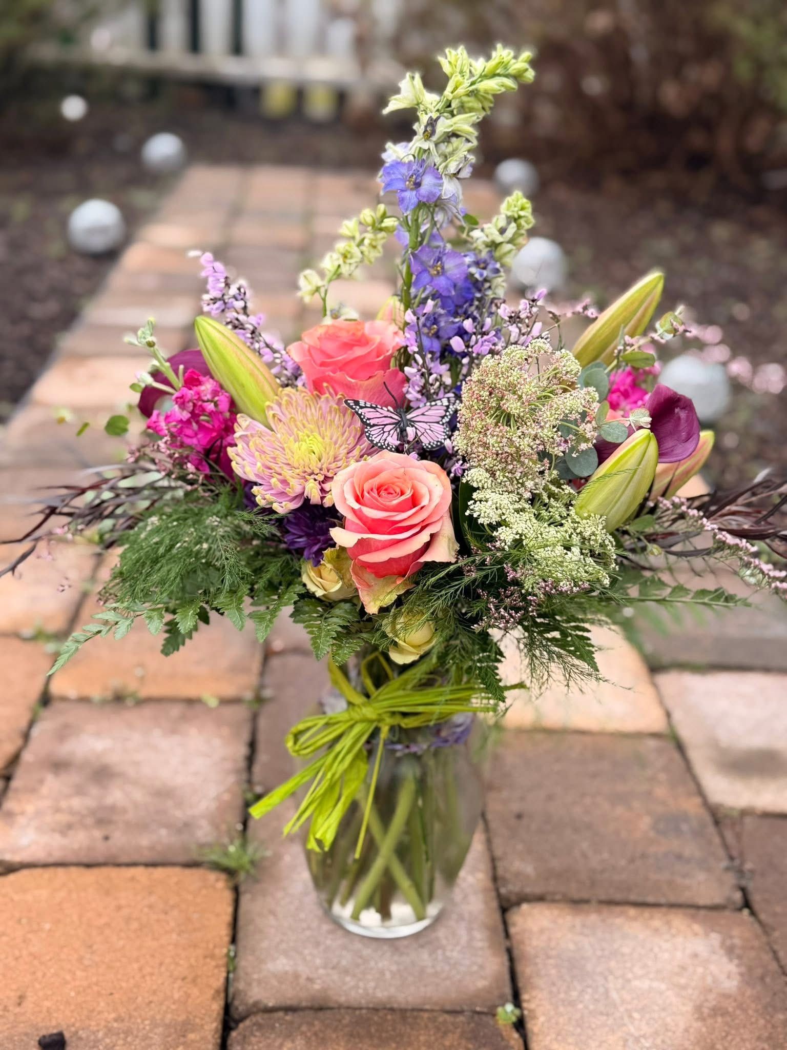 Purple rose floral arrangement in glass vase with butterfly accents on a wooden surface.