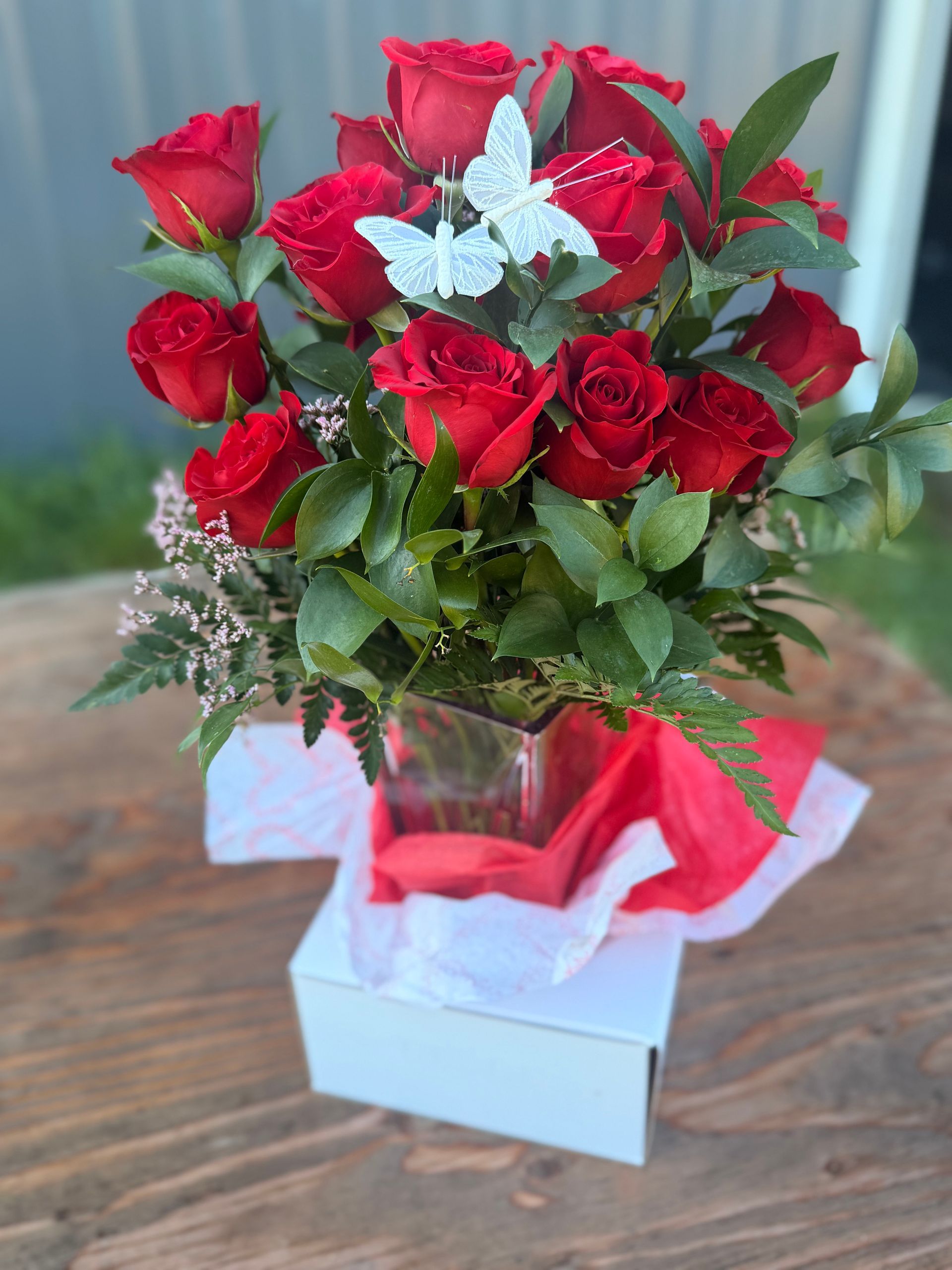 Purple rose floral arrangement in glass vase with butterfly accents on a wooden surface.