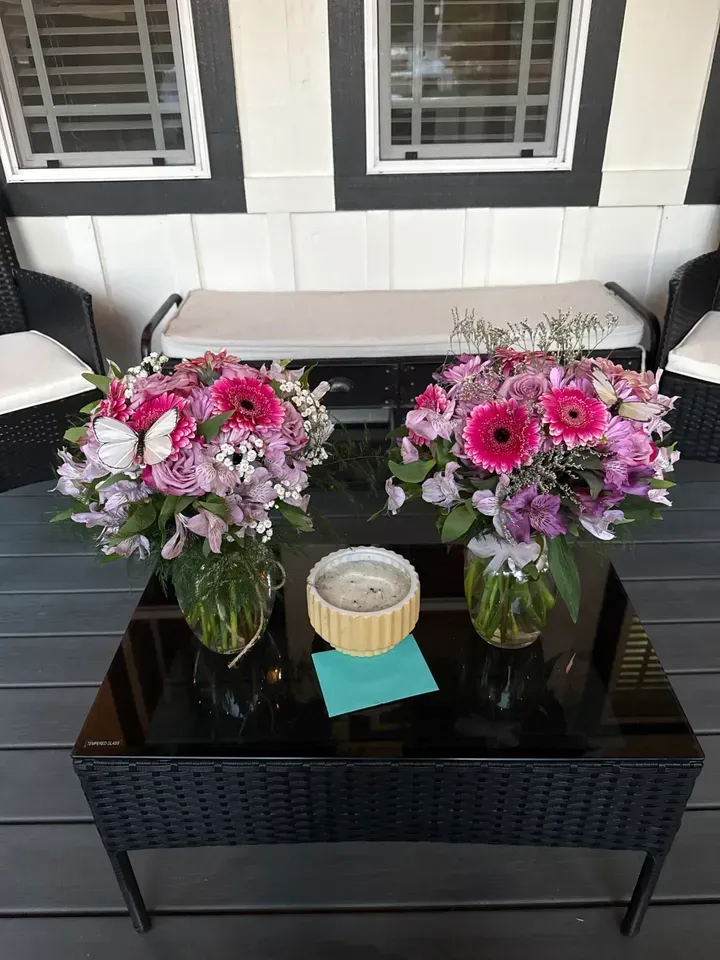 Two floral bouquets in vases sit on a black table with a candle.