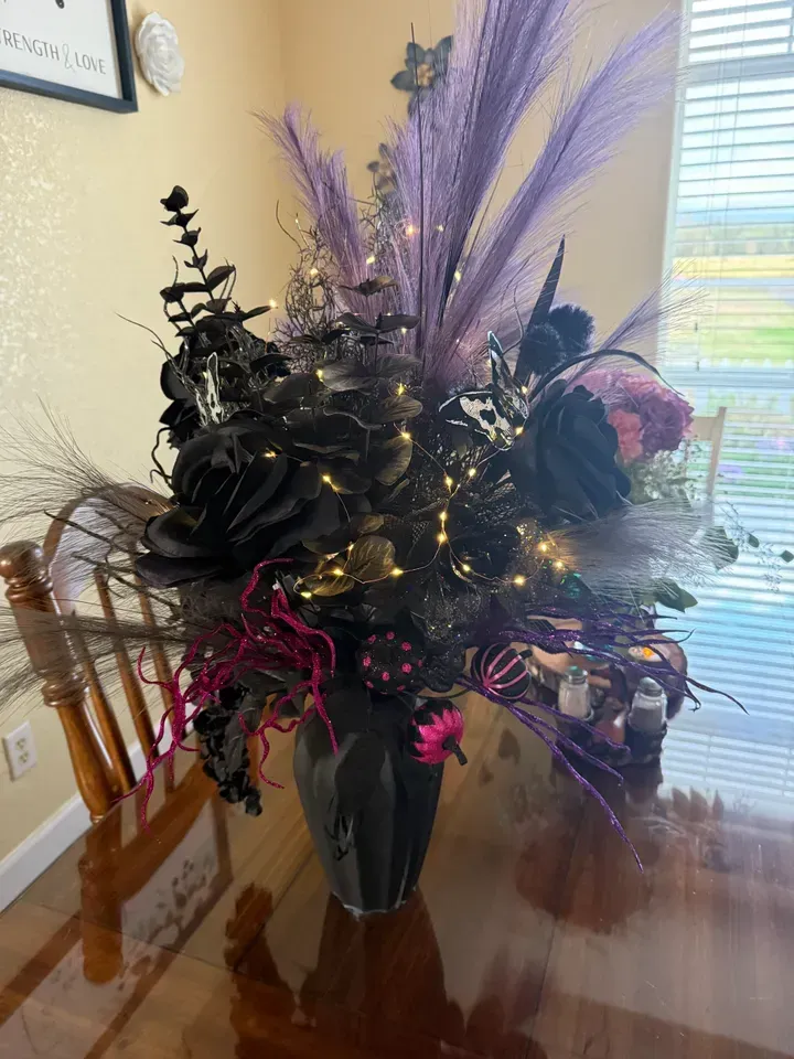 Black and purple floral arrangement in a vase on a wooden table.