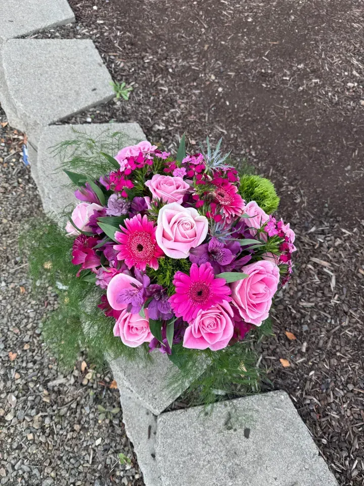 Purple rose floral arrangement in glass vase with butterfly accents on a wooden surface.