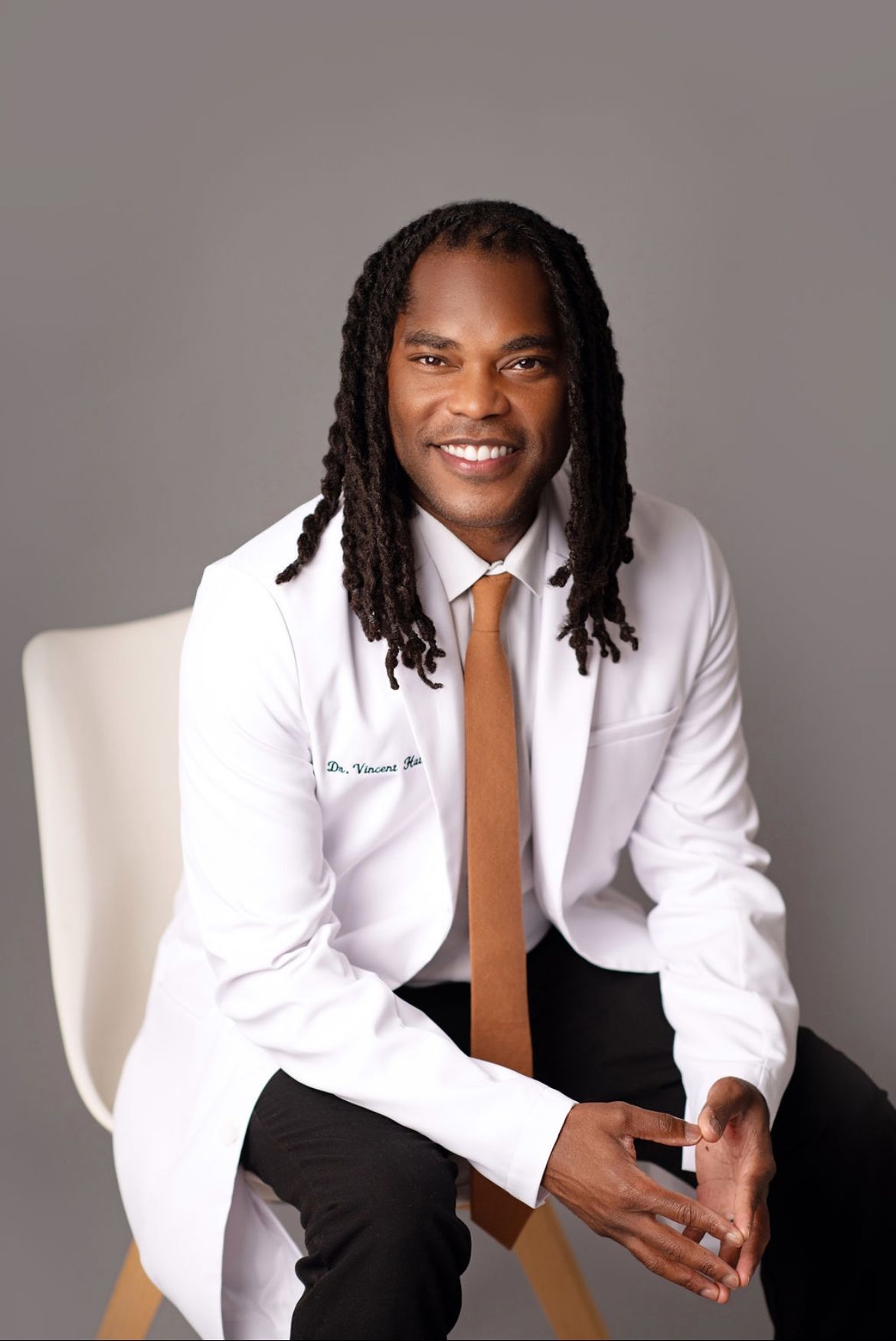 A man in a white coat and tie is sitting in a chair.