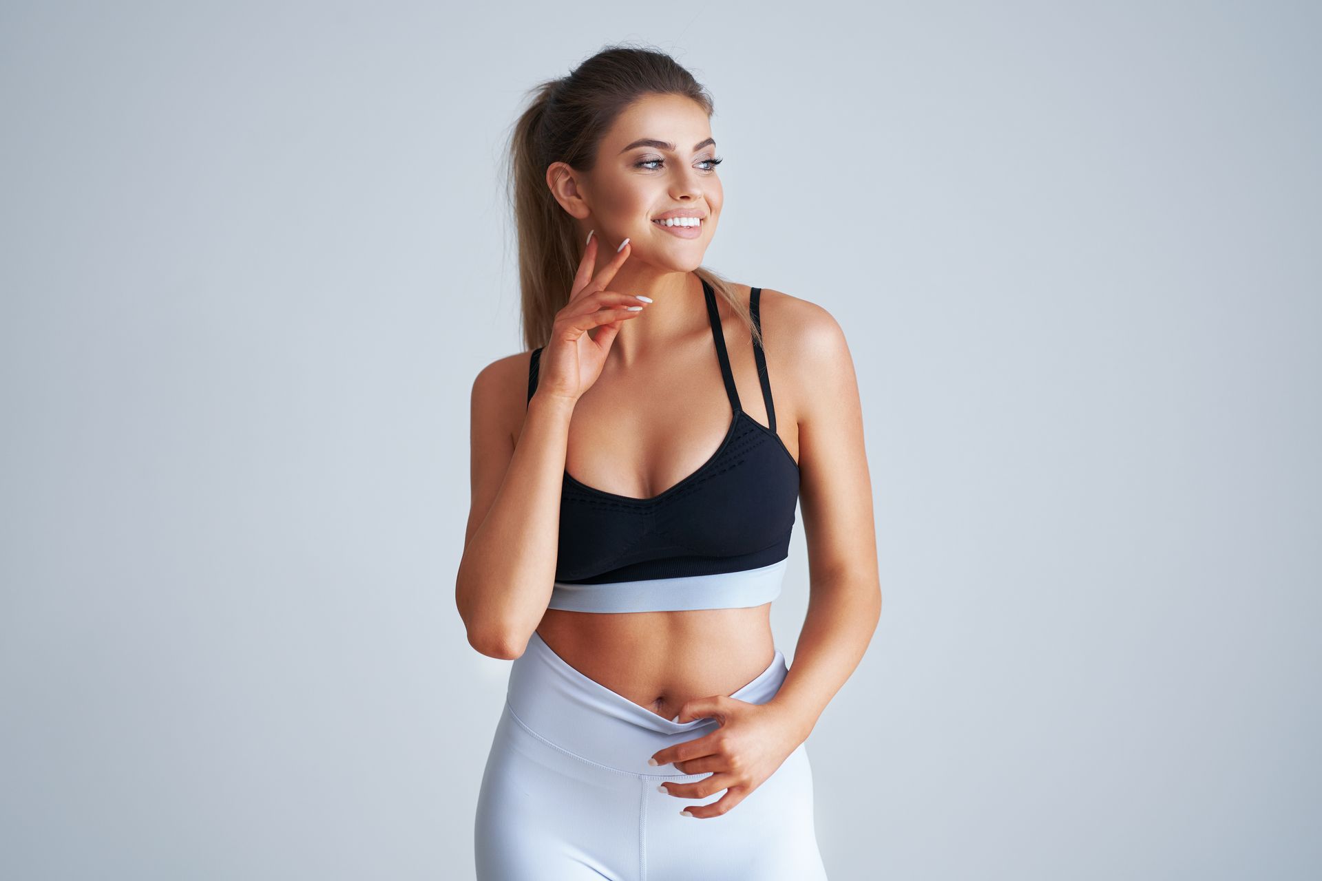 A woman in a black sports bra and white pants is smiling.