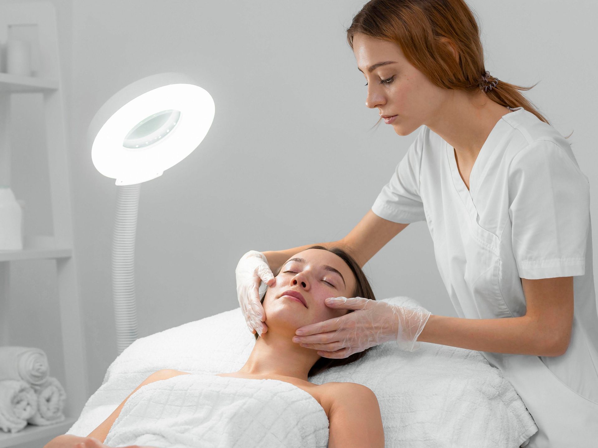 A woman is laying on a bed getting a facial treatment from a nurse.