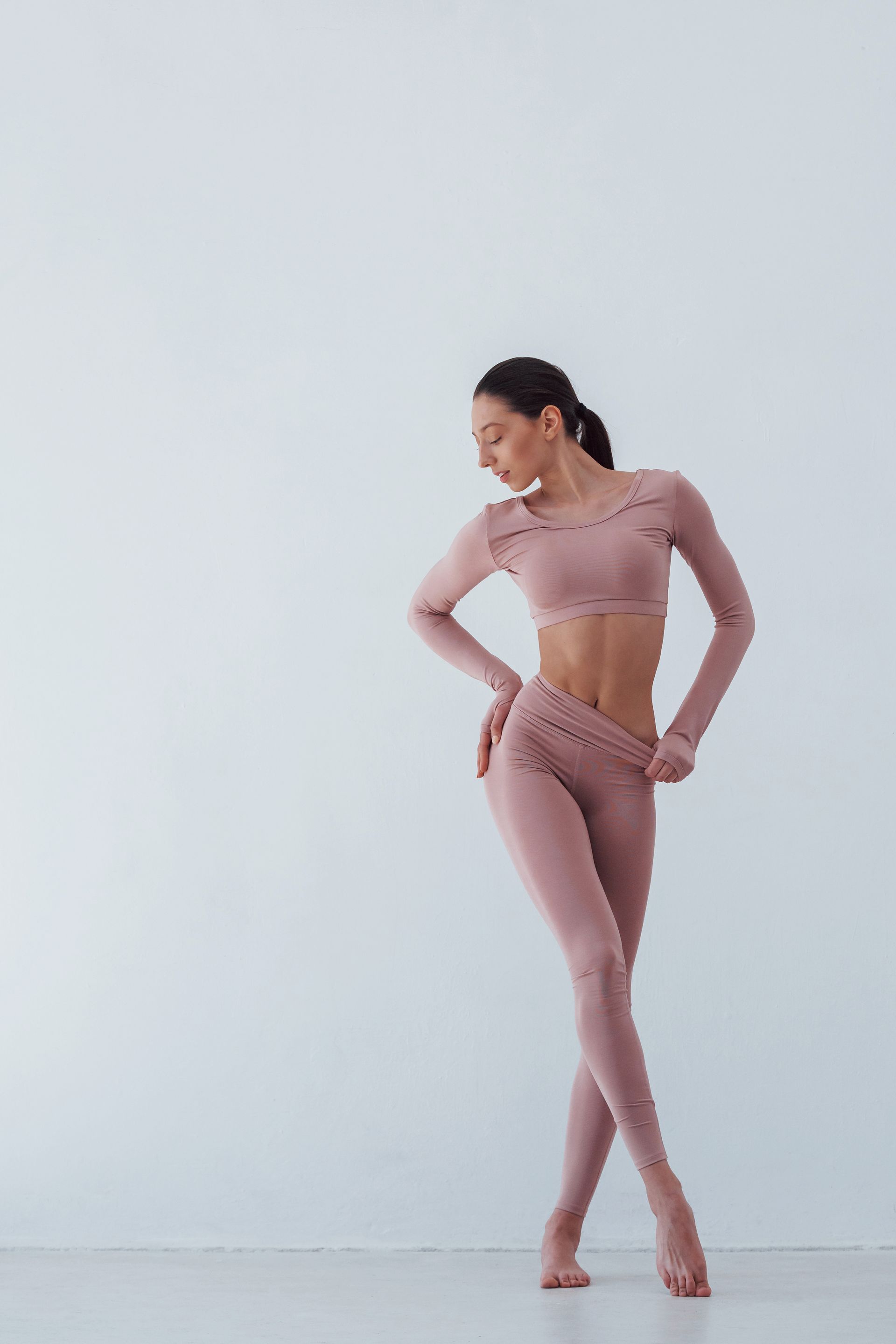 A woman in a pink crop top and leggings is standing with her hands on her hips.