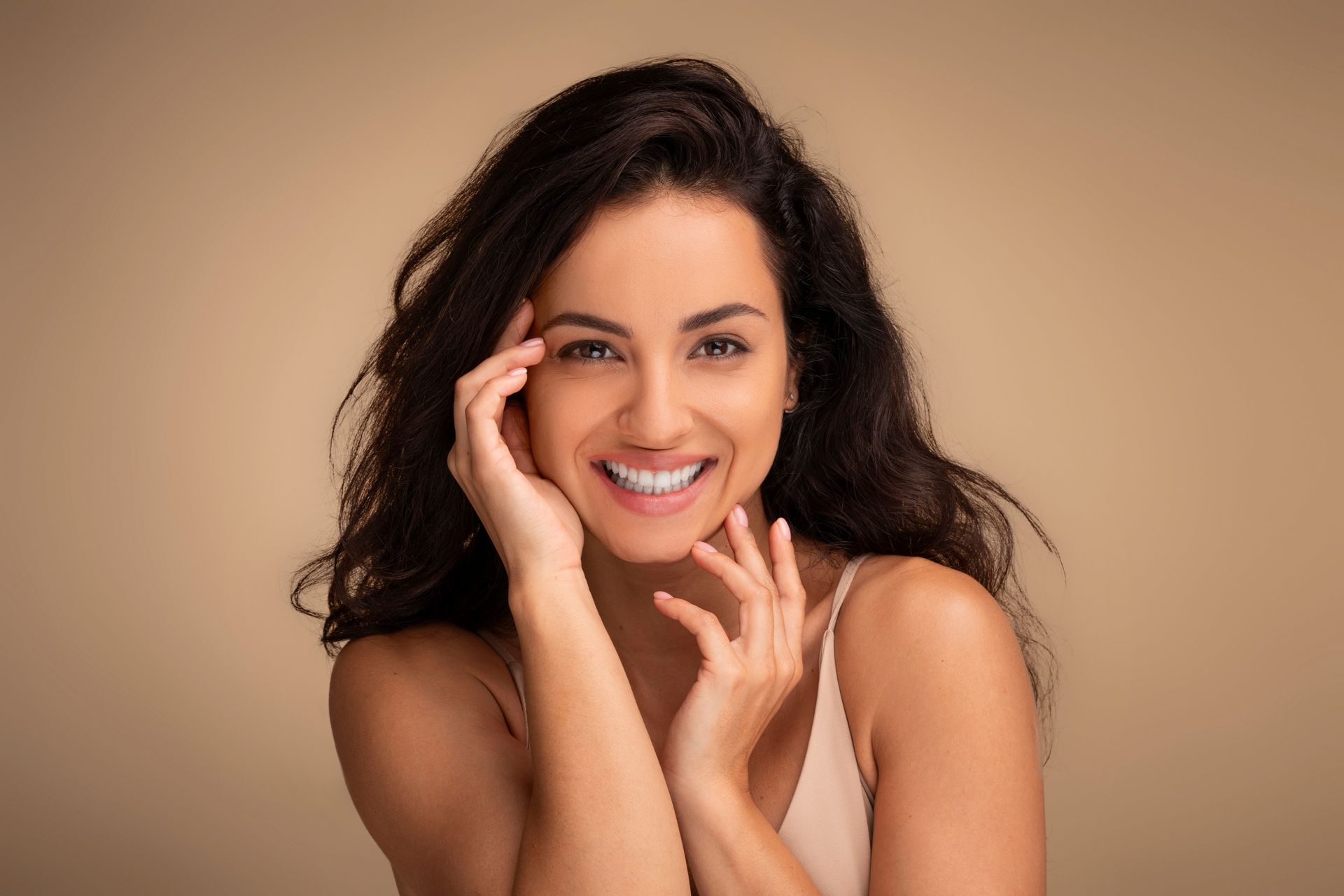 A woman is smiling and touching her face with her hands.