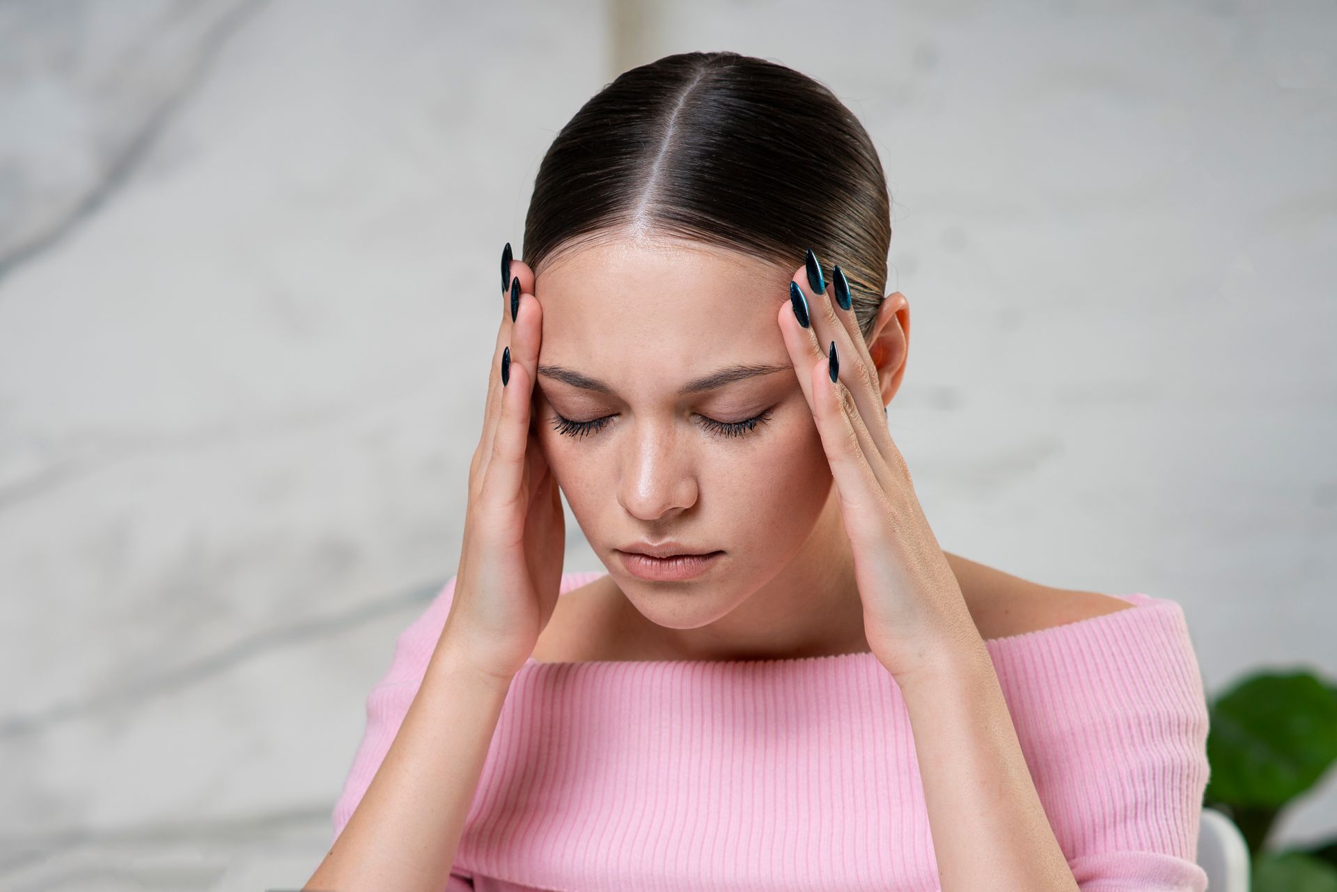 A woman in a pink sweater is holding her head with her hands.