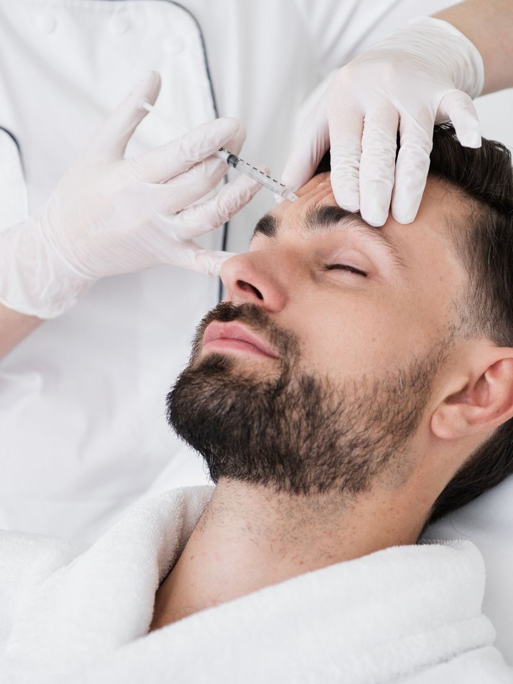 Man receiving Botox injection in his forehead; hands in gloves, doctor's office.