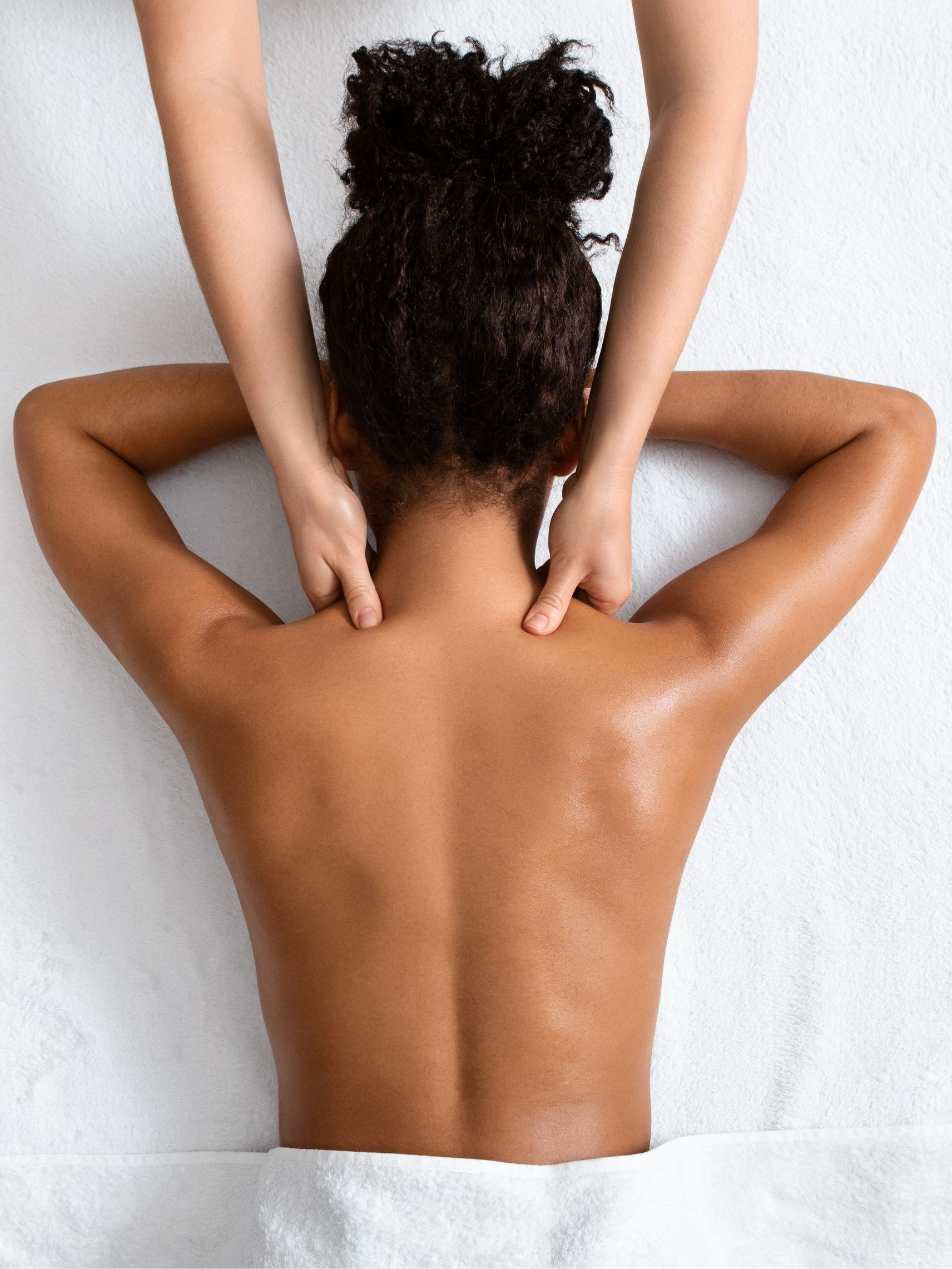 Person receiving a back and shoulder massage, lying on a white surface. Hands massaging shoulders.