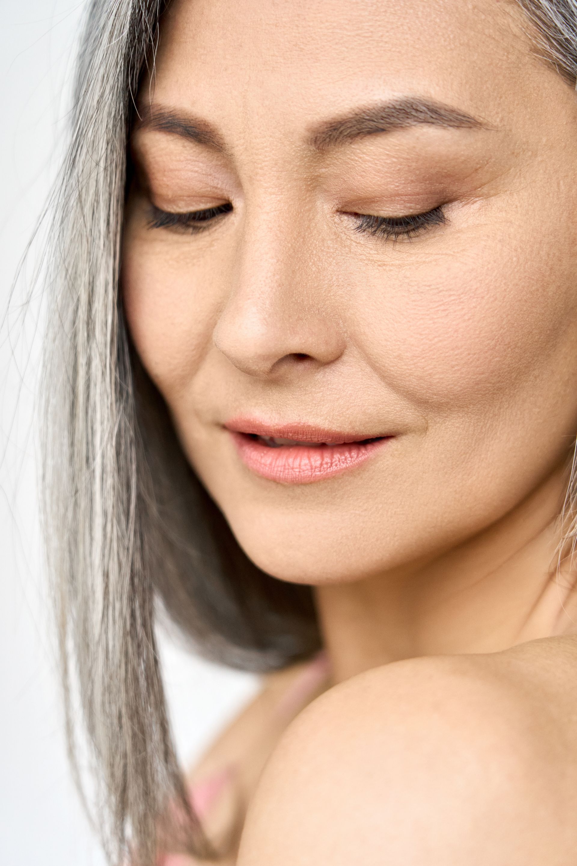 Woman with silver hair, eyes closed, smiling gently, bare shoulders, soft lighting.