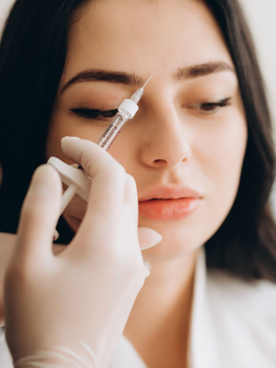 Person receiving an injection in the eyebrow, held by gloved hand.