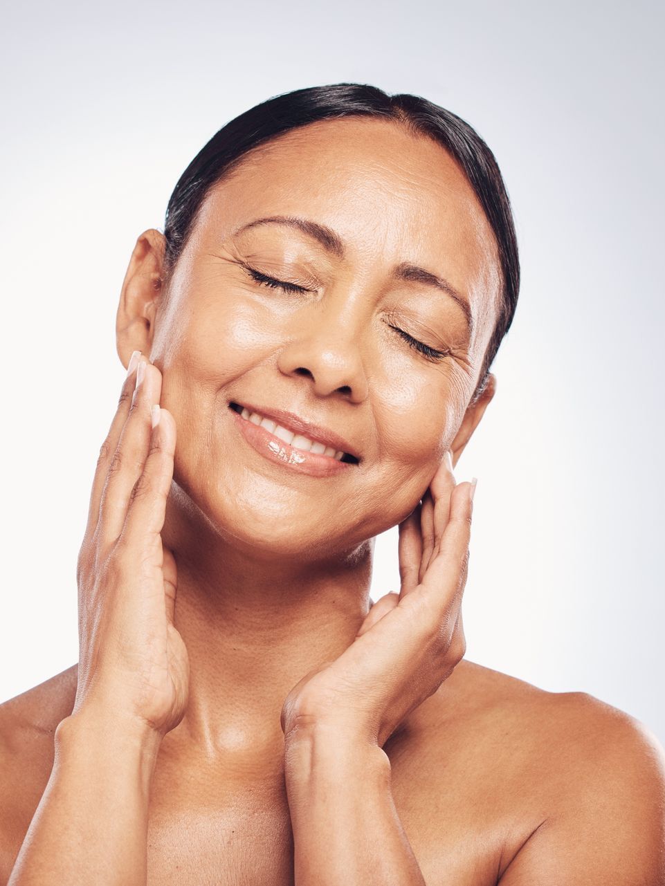 A woman is touching her face with her hands and smiling.