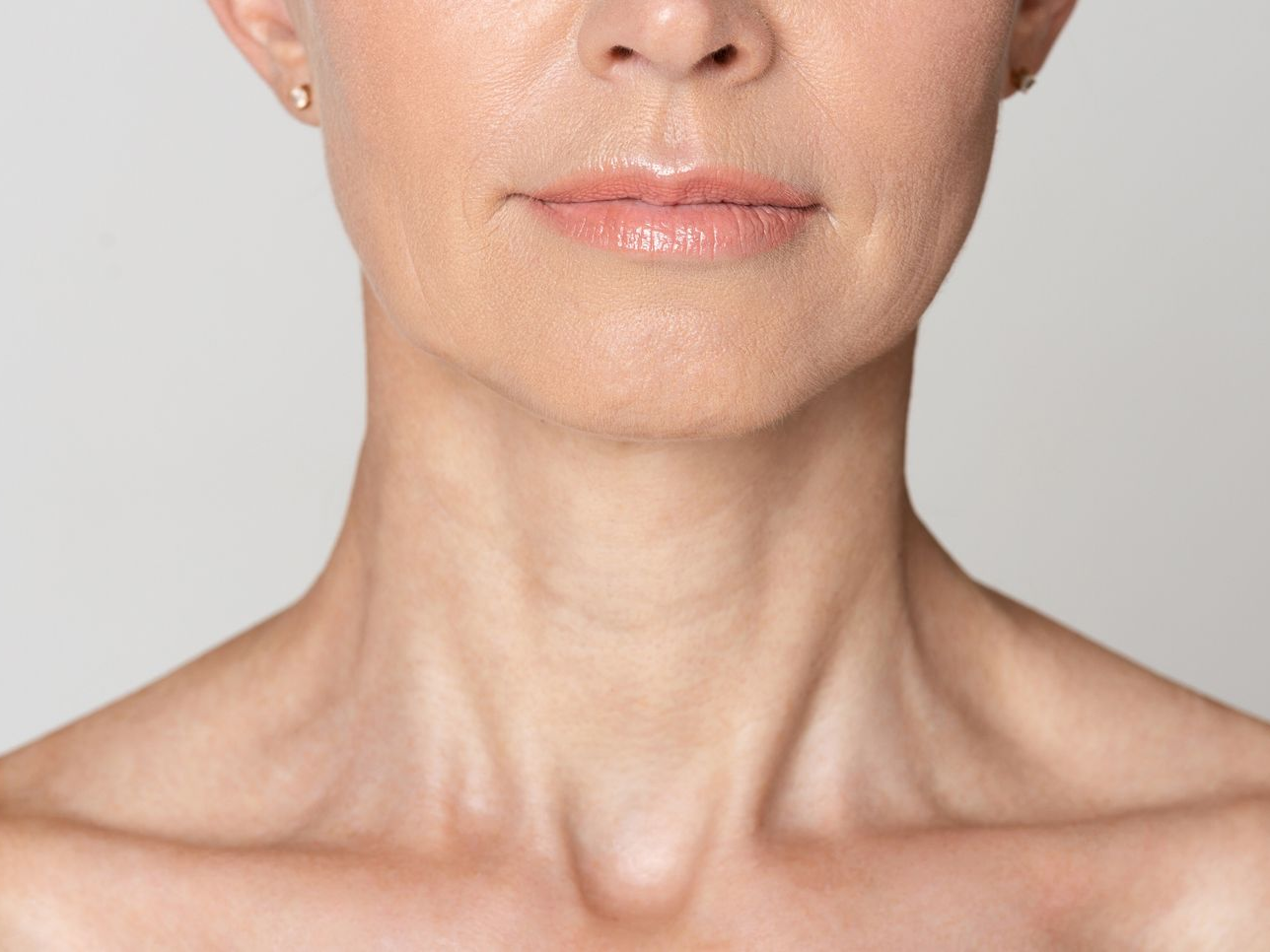 Close-up of a person's neck and lower face, showing skin texture with subtle wrinkles and defined collarbones.