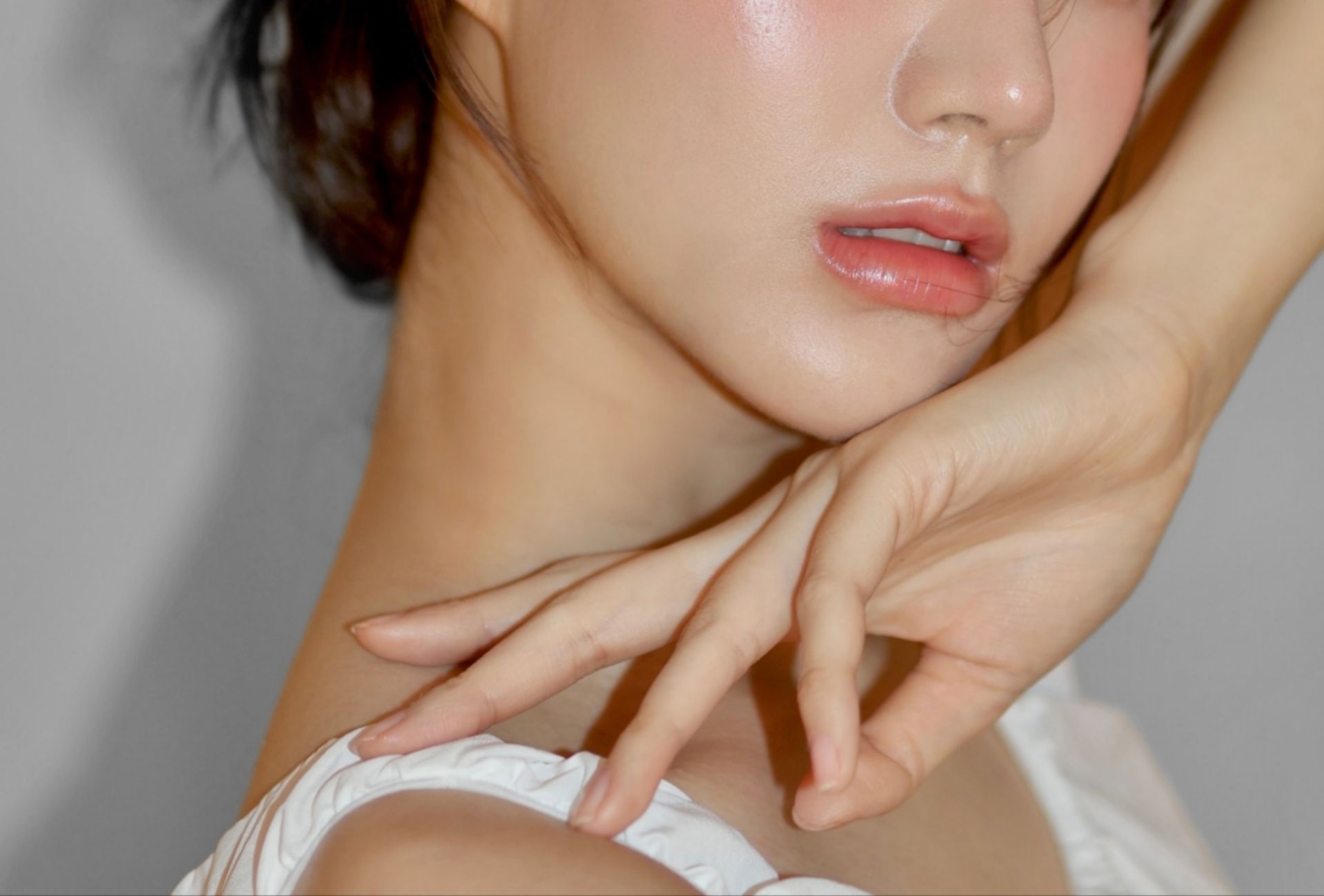 Woman with pale skin, hand near face, gazing upward. Highlighted skin, light-colored clothing.