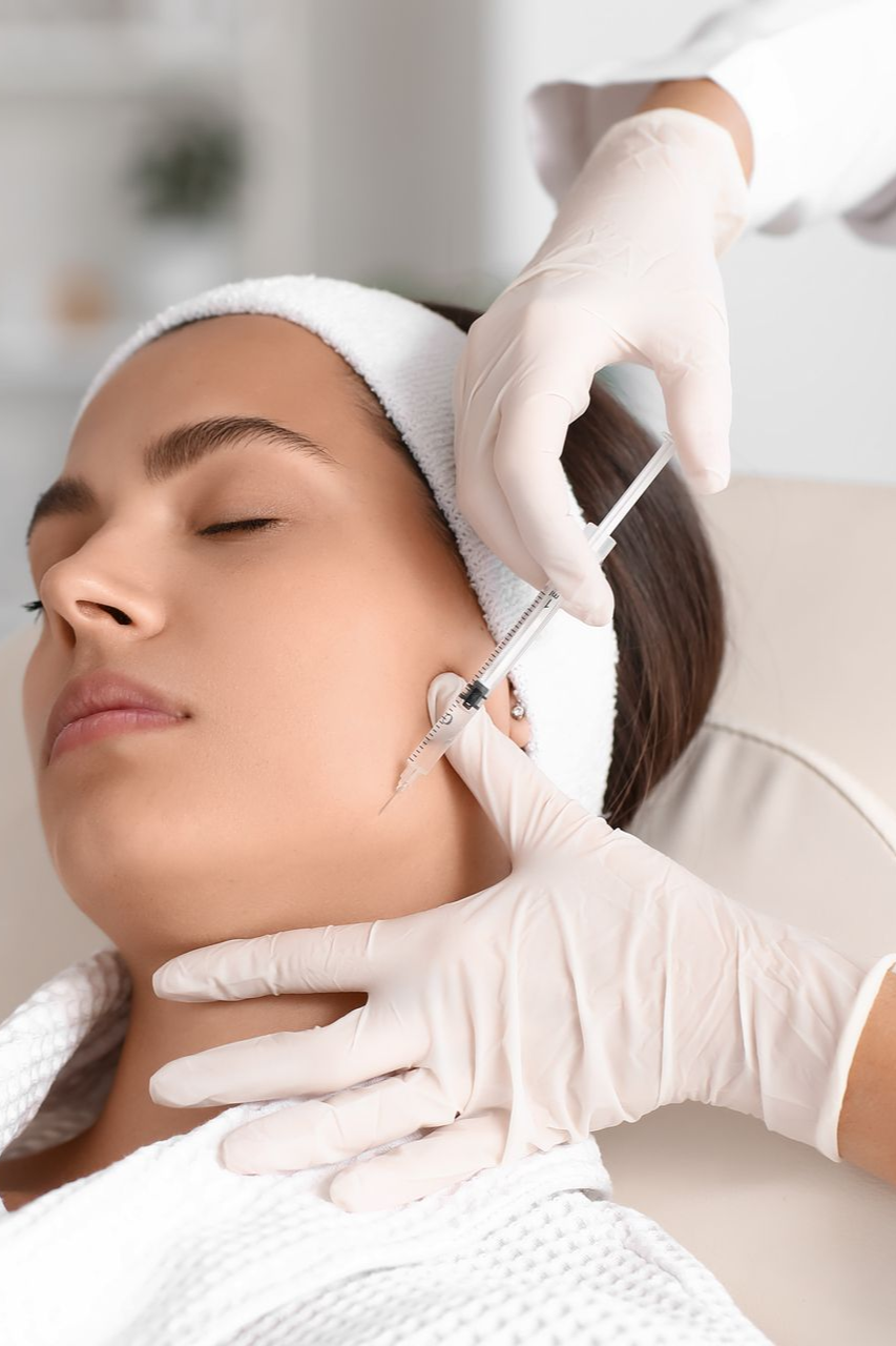 Person receiving a facial injection. White-gloved hand injecting near cheekbone. Setting appears to be a medical office.