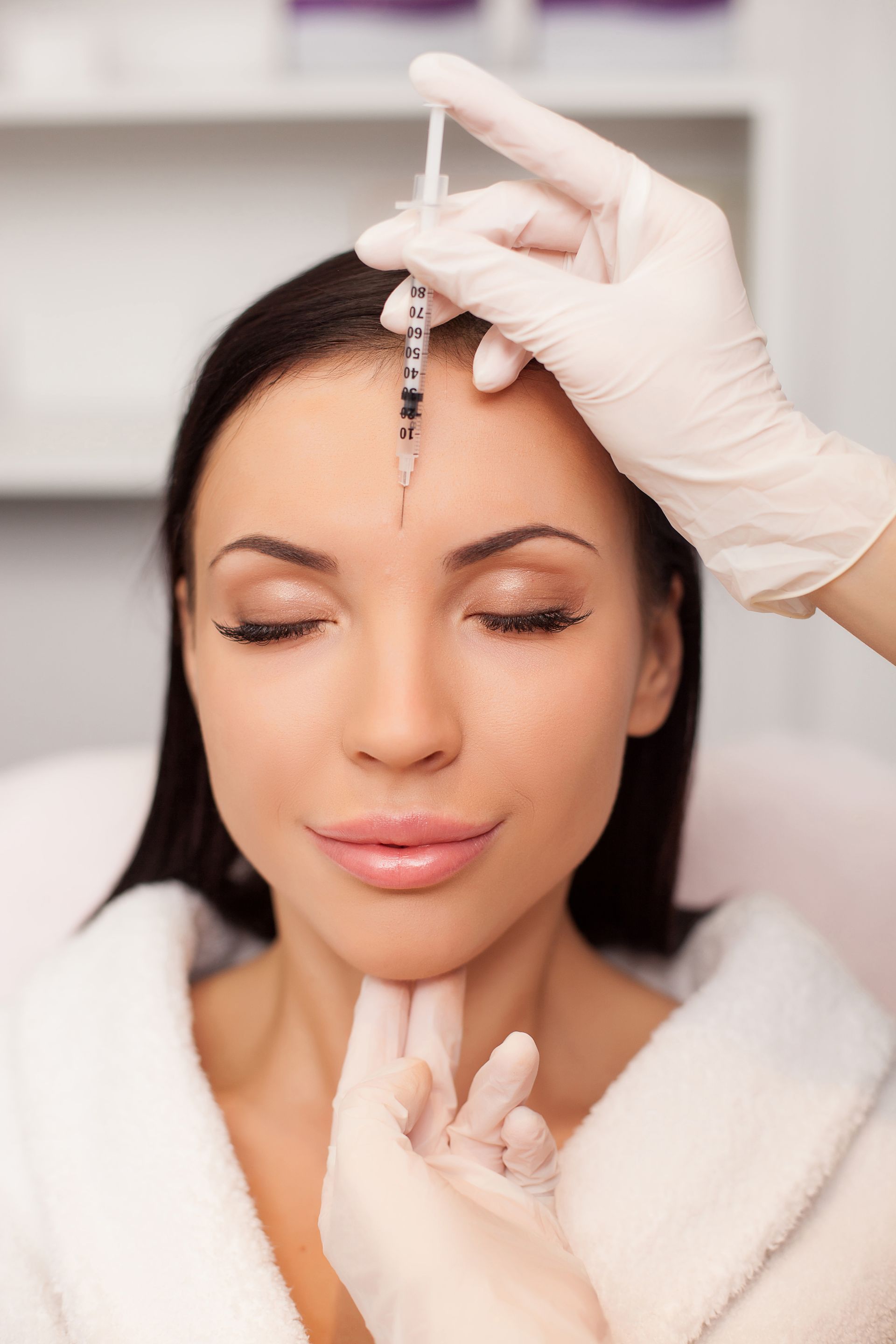 Woman receiving an injection in her forehead. Gloved hands hold the syringe. Her eyes are closed.